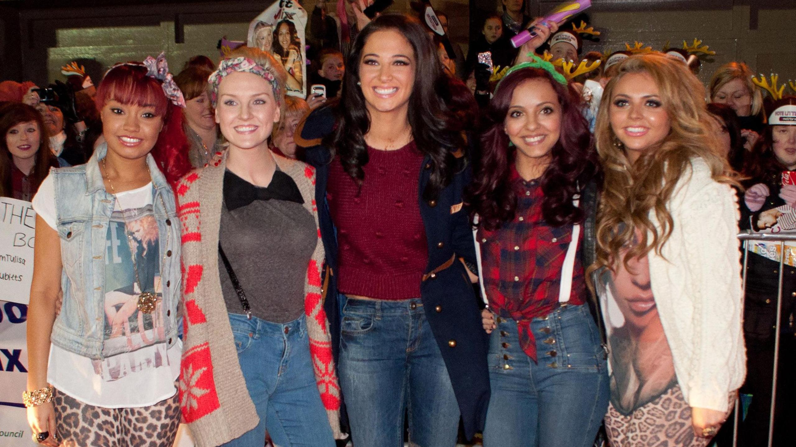 Little Mix pictured with X-Factor judge Tulisa Contostavolos in 2011. Jade is wearing a red checked shirt, high waisted jeans, white braces and a green headband. 