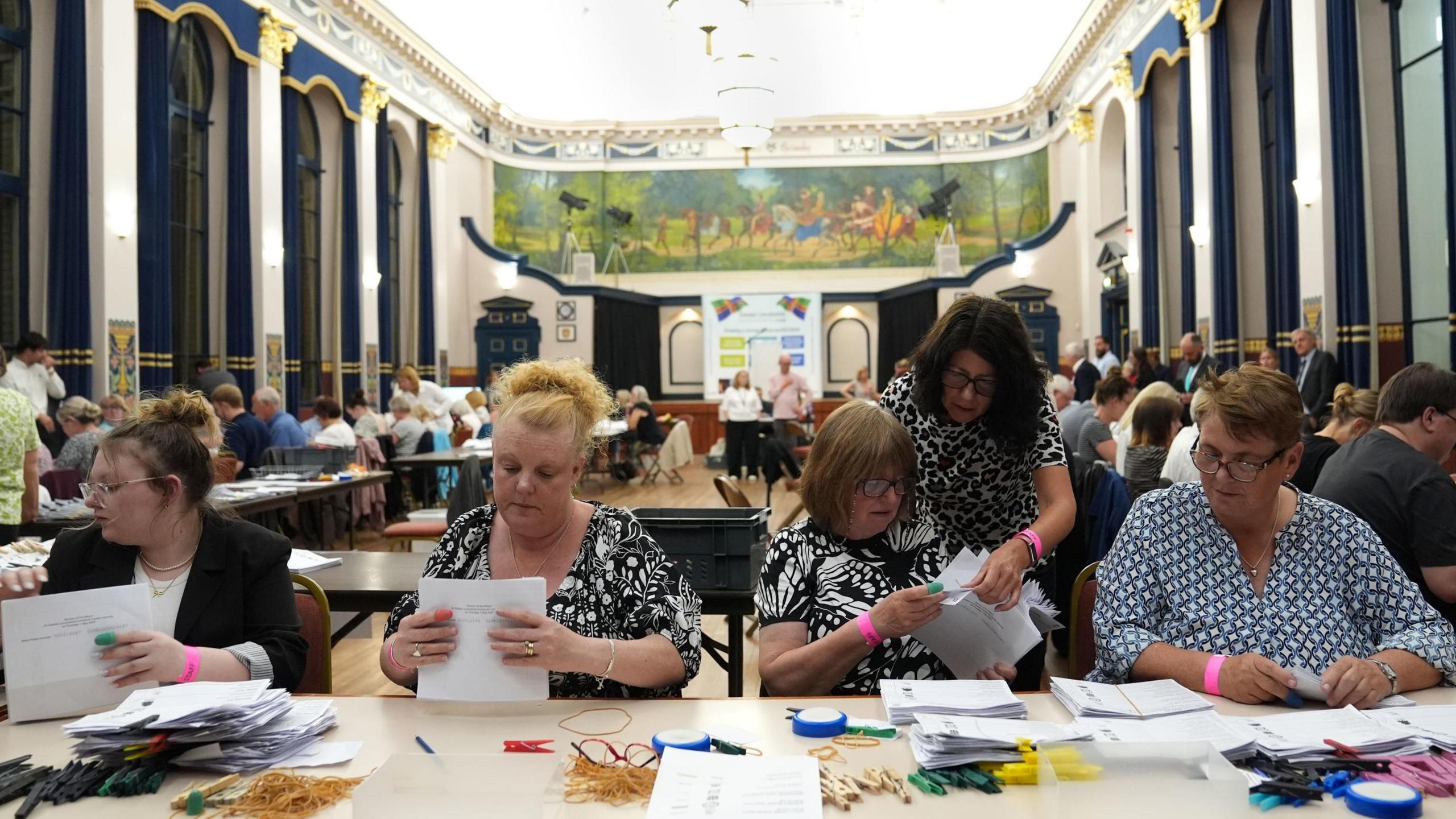 Four women sit at a table in a town hall counting votes