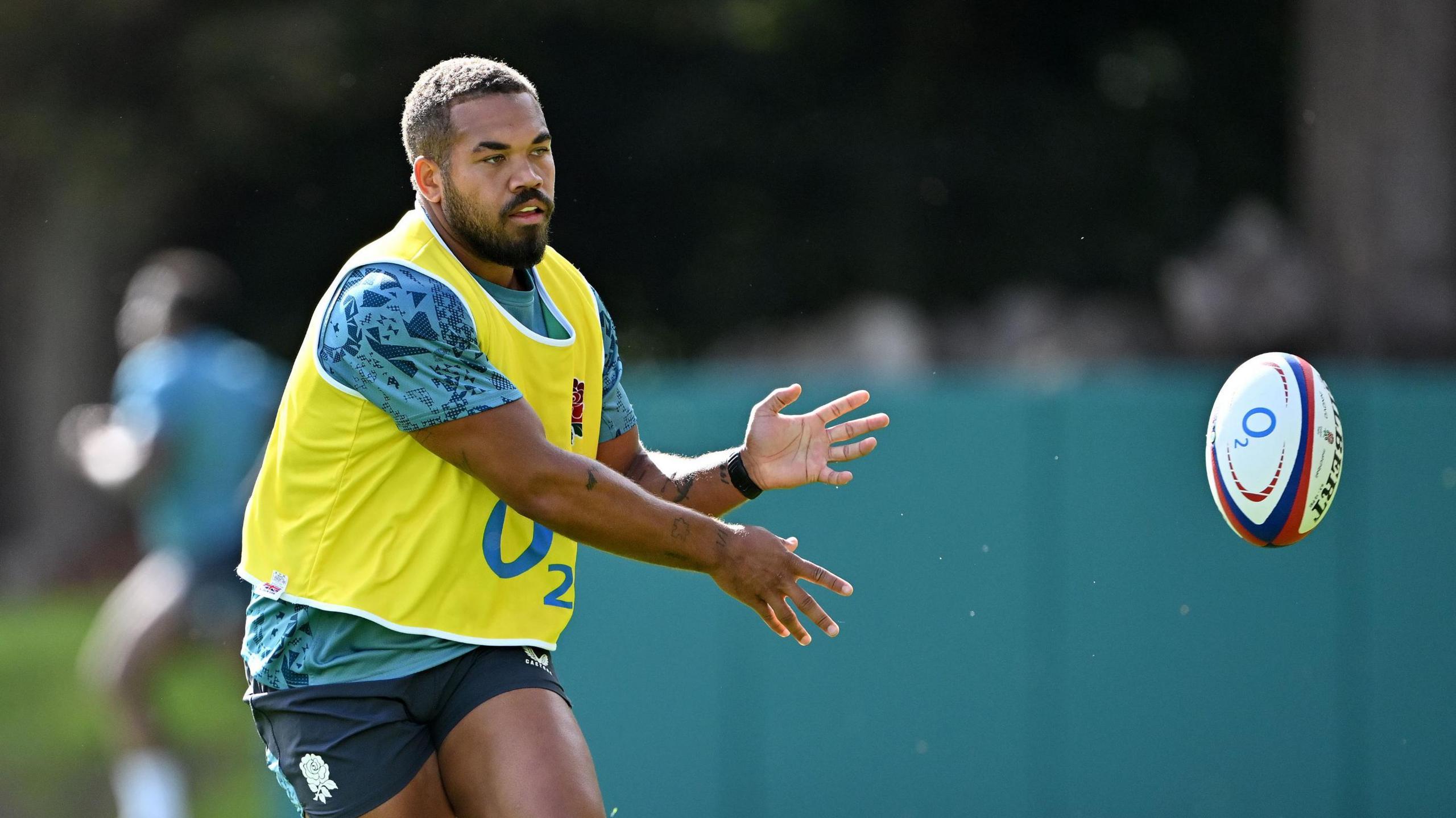 Ollie Lawrence throws the ball to his left and holds his arms out to his side during a training session with England
