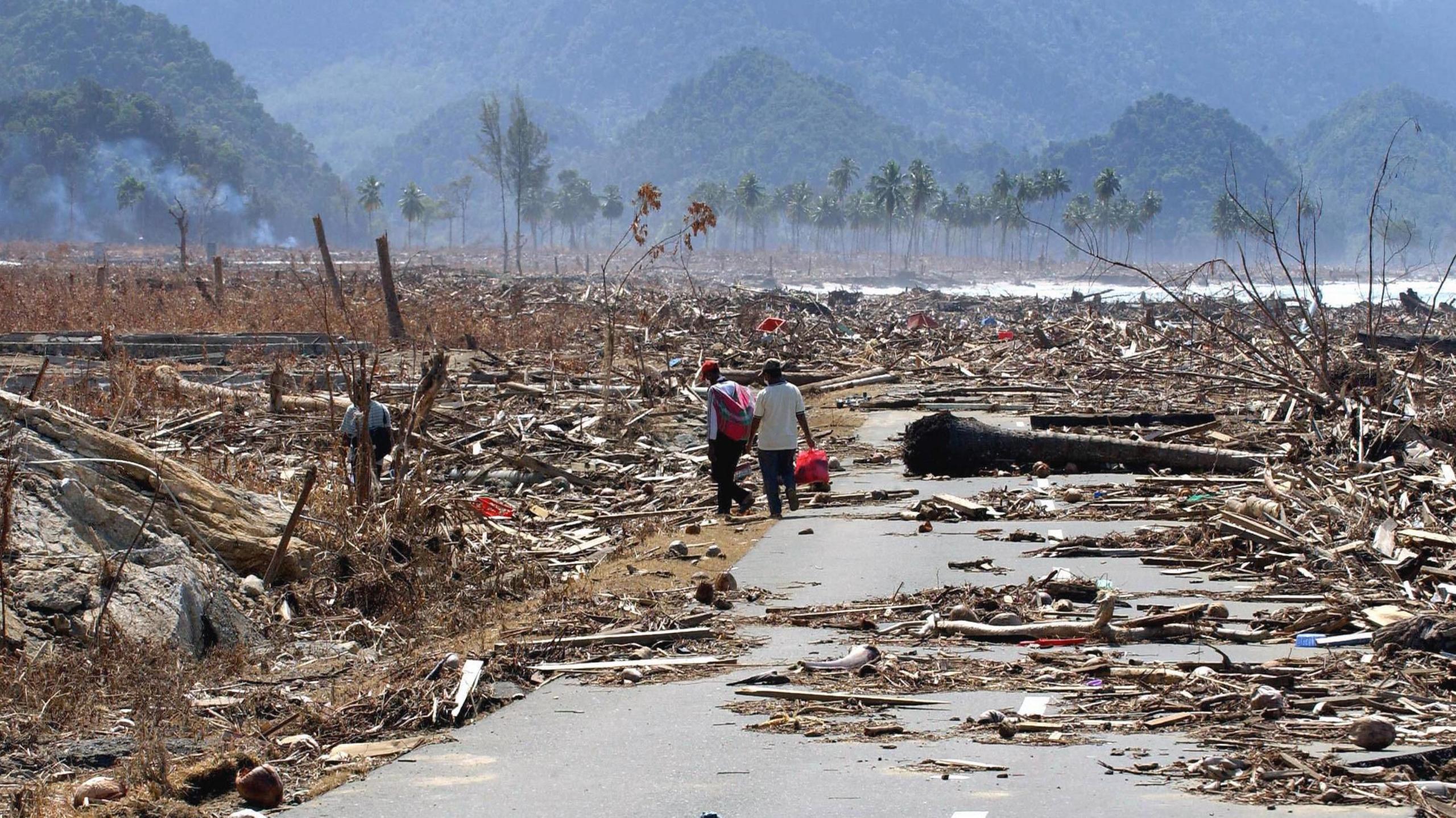 Two Indonesian refugees walk down a road covered with debris leftover from the tsunami disaster, as they return to look for their homes in the west coast town of Leupung.