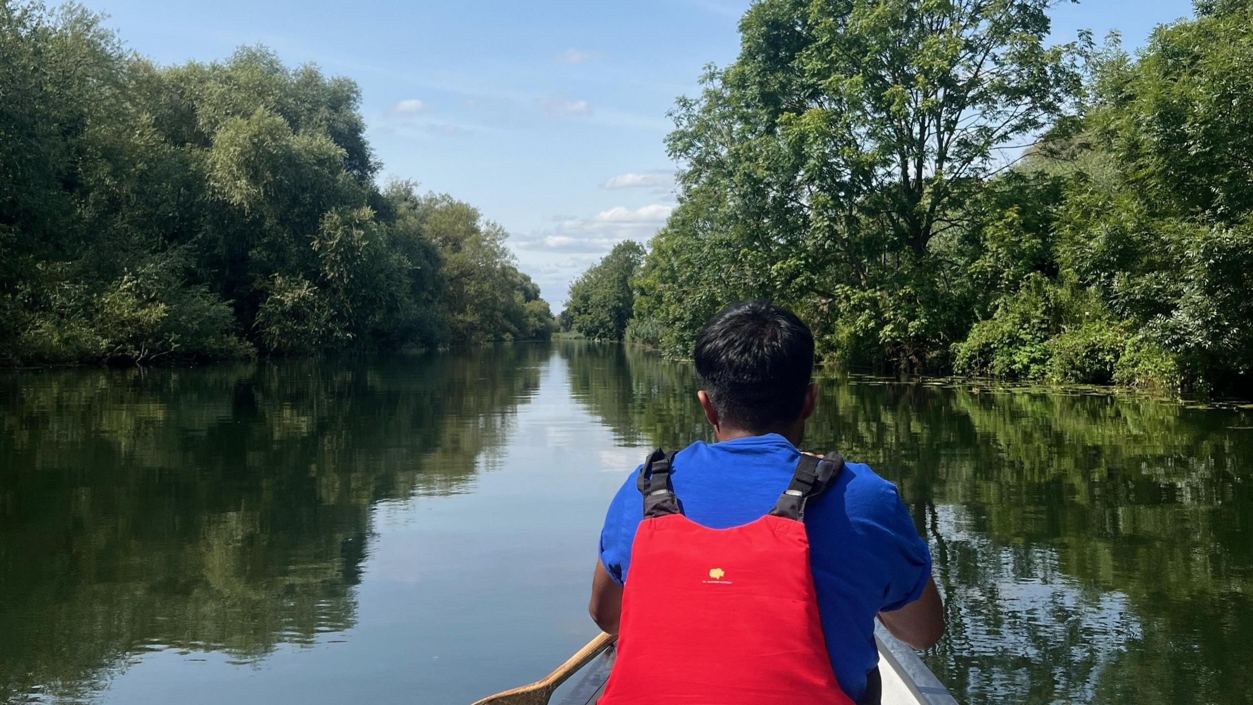 Boy in a boat on a river surrounded by trees