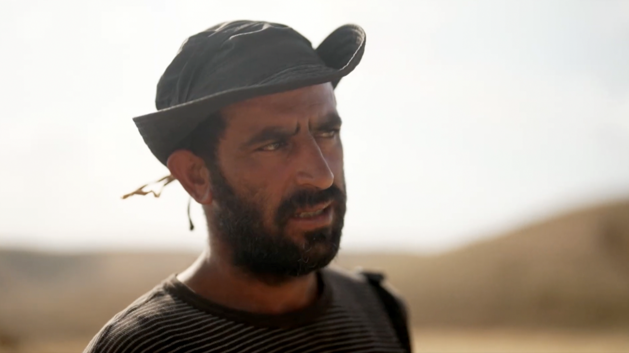 Ahmad Daraghme pictured from the shoulders up with the background out of focus. He is wearing a hat and a dark beard and looking off camera to his left.