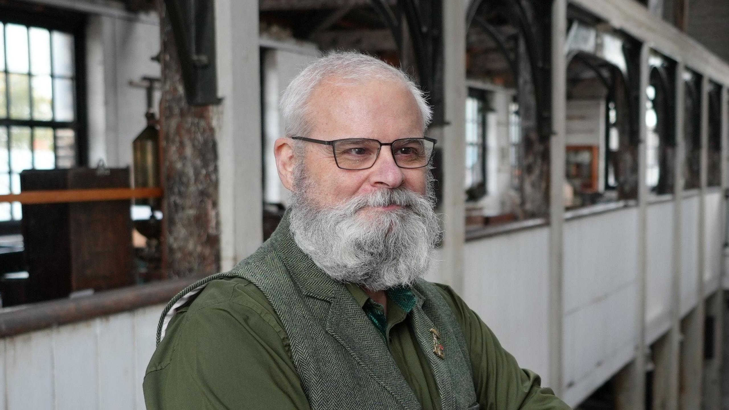 Fraser Hale looks to the right of the image and smiles. He stands in the museum's first floor that overlooks the lower floor. 