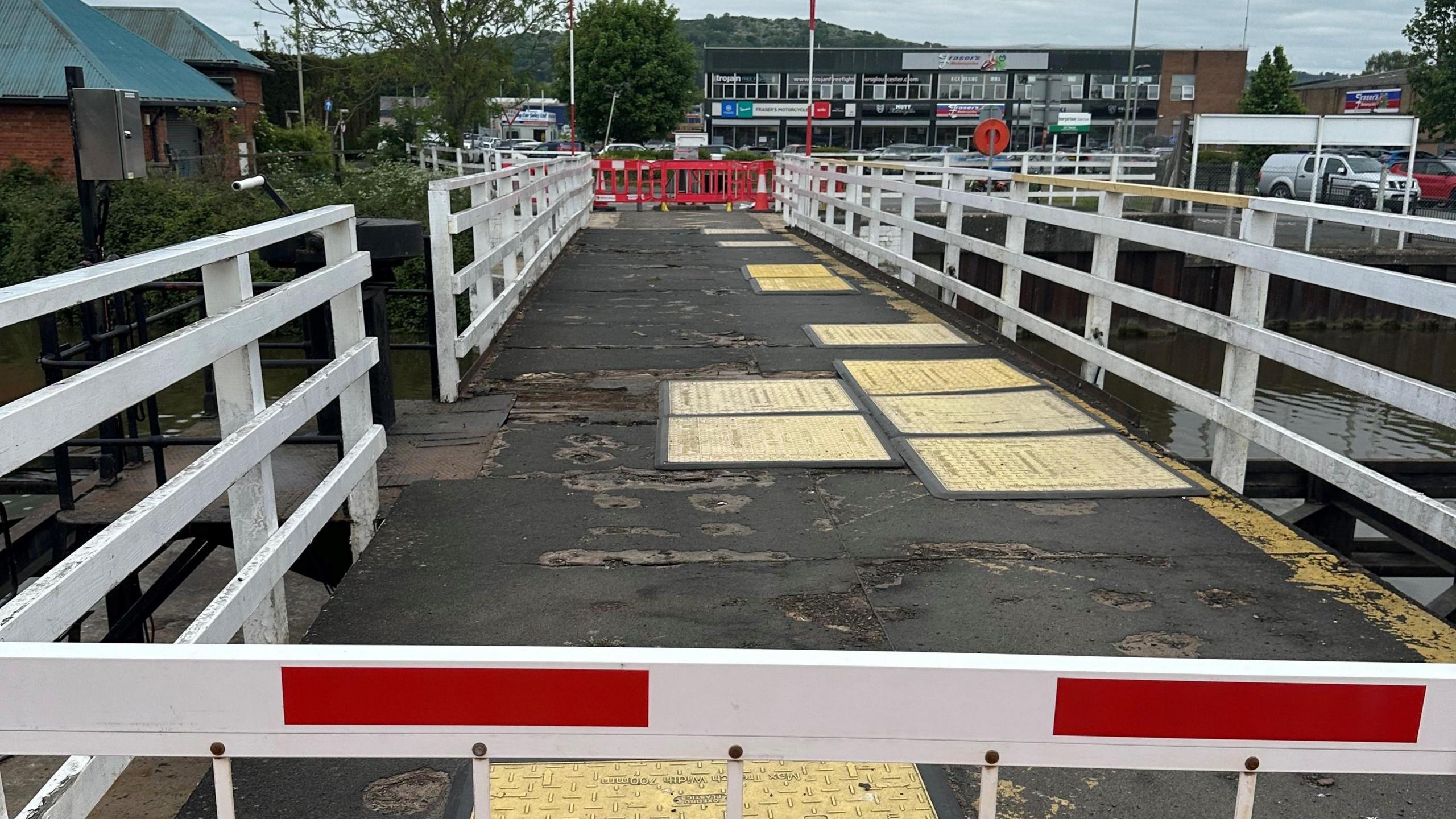 Image of Hempsted Bridge, with safety mats over the bumps in the tarmac. Red barriers block either side of the bridge.