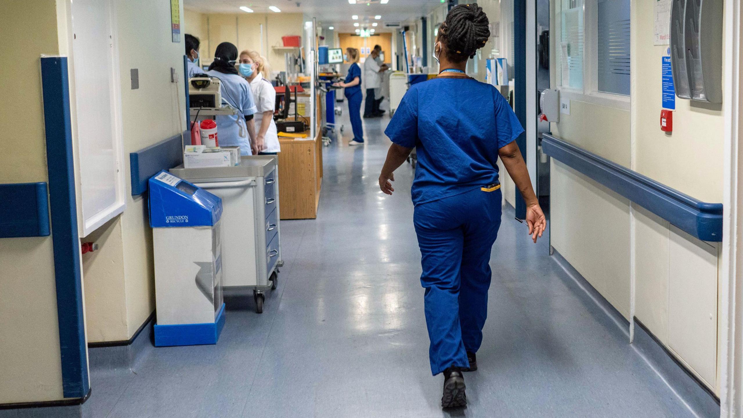 Woman in hospital scrubs walking away down a hospital corridor.