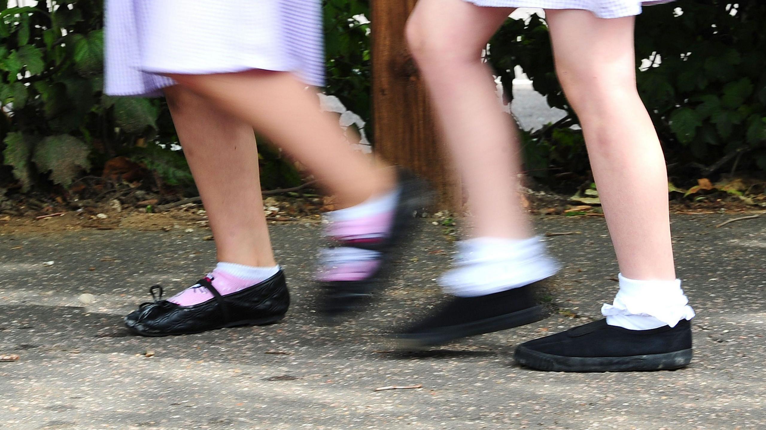 Two schoolgirls running. You can see black school shoes and frilly white socks.