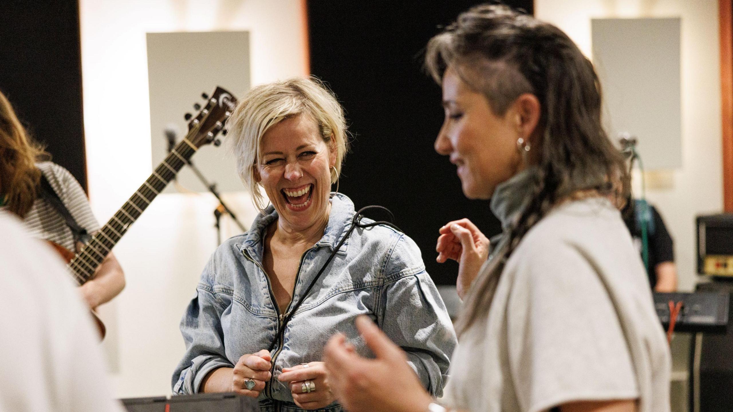 Cora Bissett has grey, long-ish hair and is wearing a vintage denim jacket. She is laughing