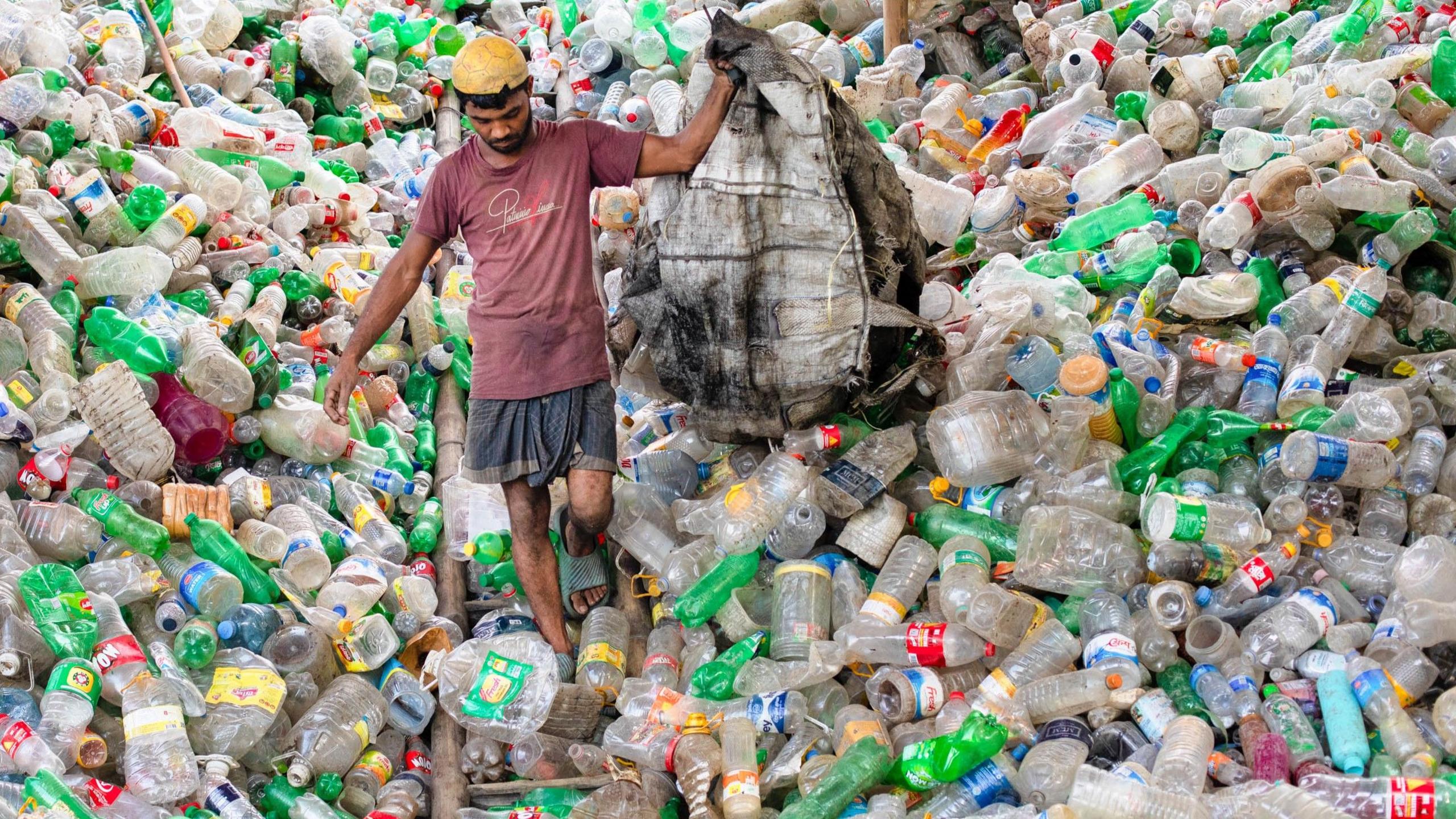 A man walks down a massive pile of plastic bottles in Bangladesh