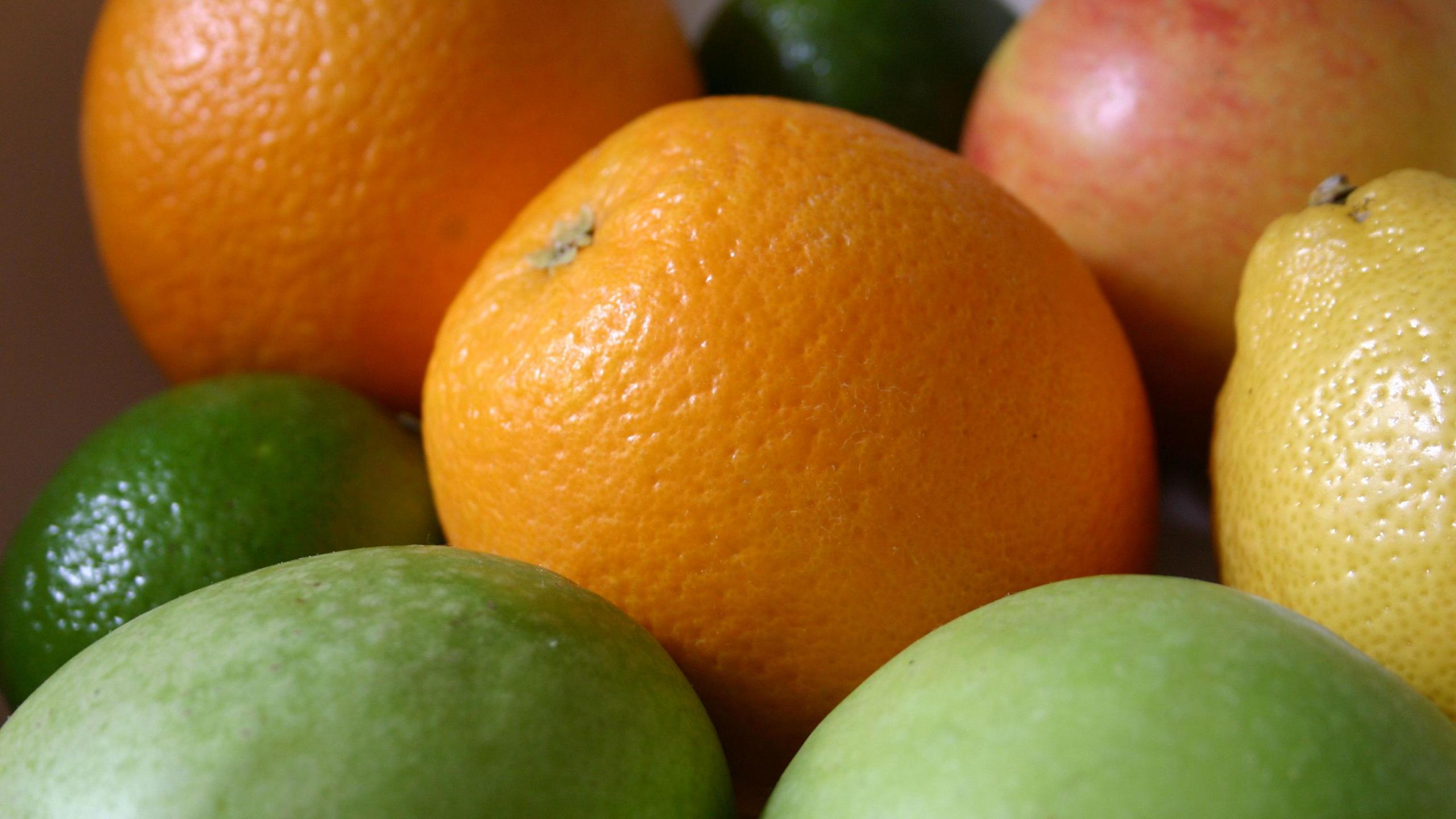 A fruit bowl with an orange at the centre, an apple in the top right, another orange in the top left and limes and lemons at the foreground.