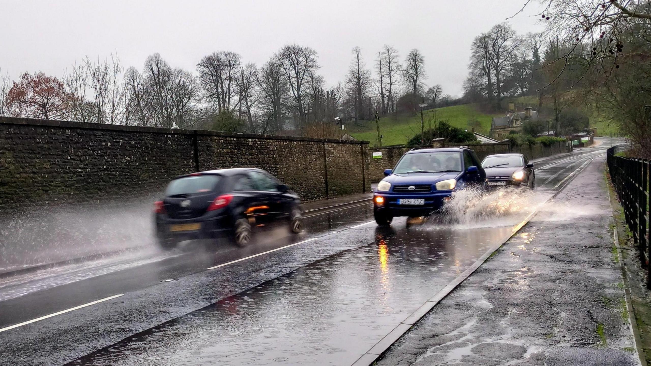 A photo of cars driving through large puddles on a road
