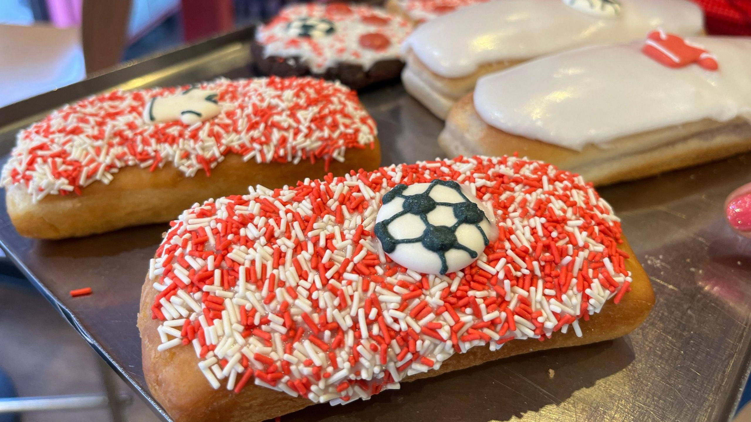 An iced bun with red and white sprinkles and a football icing design