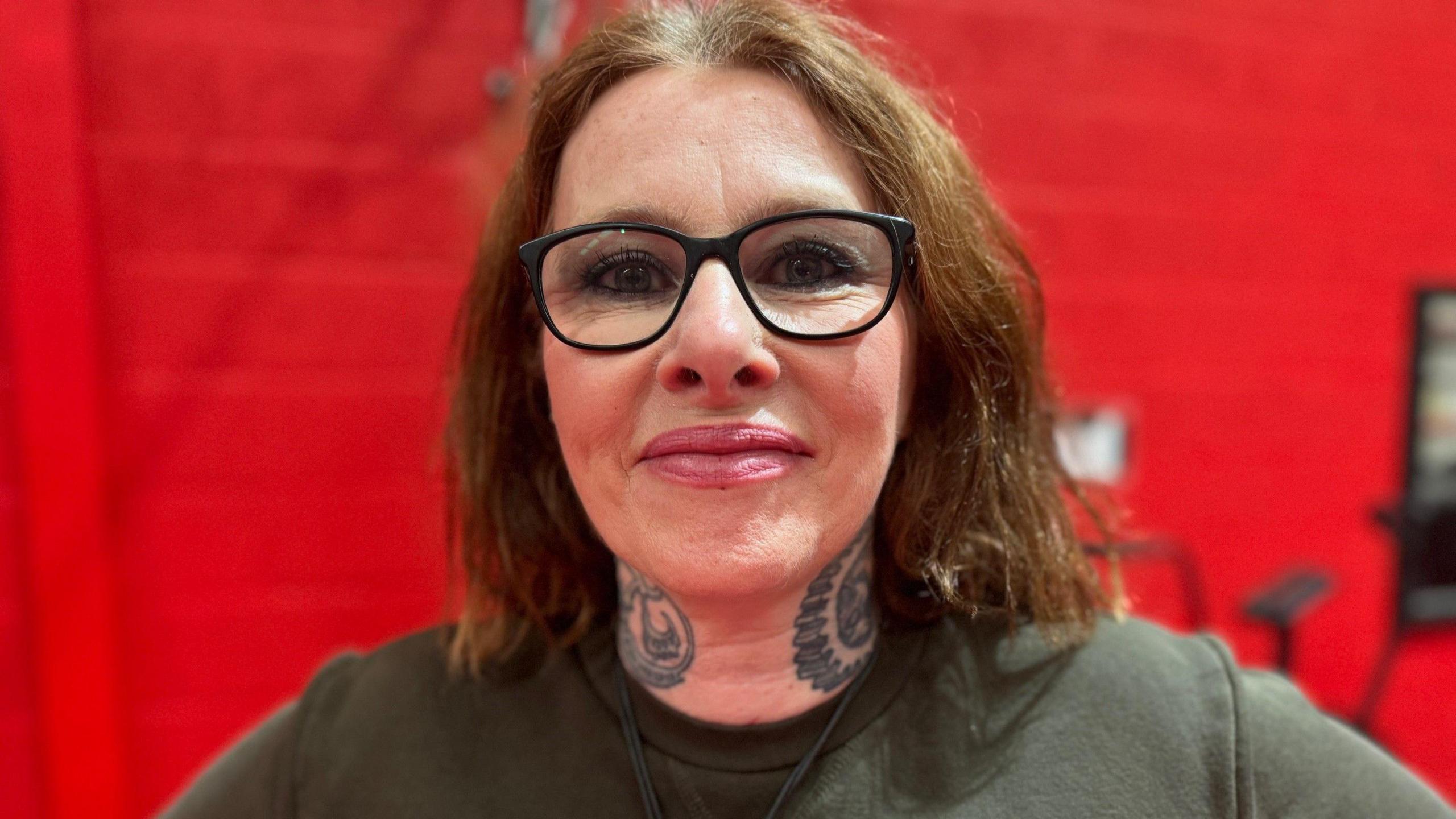 A woman wearing glasses and a dark green top stood in a room with a red background