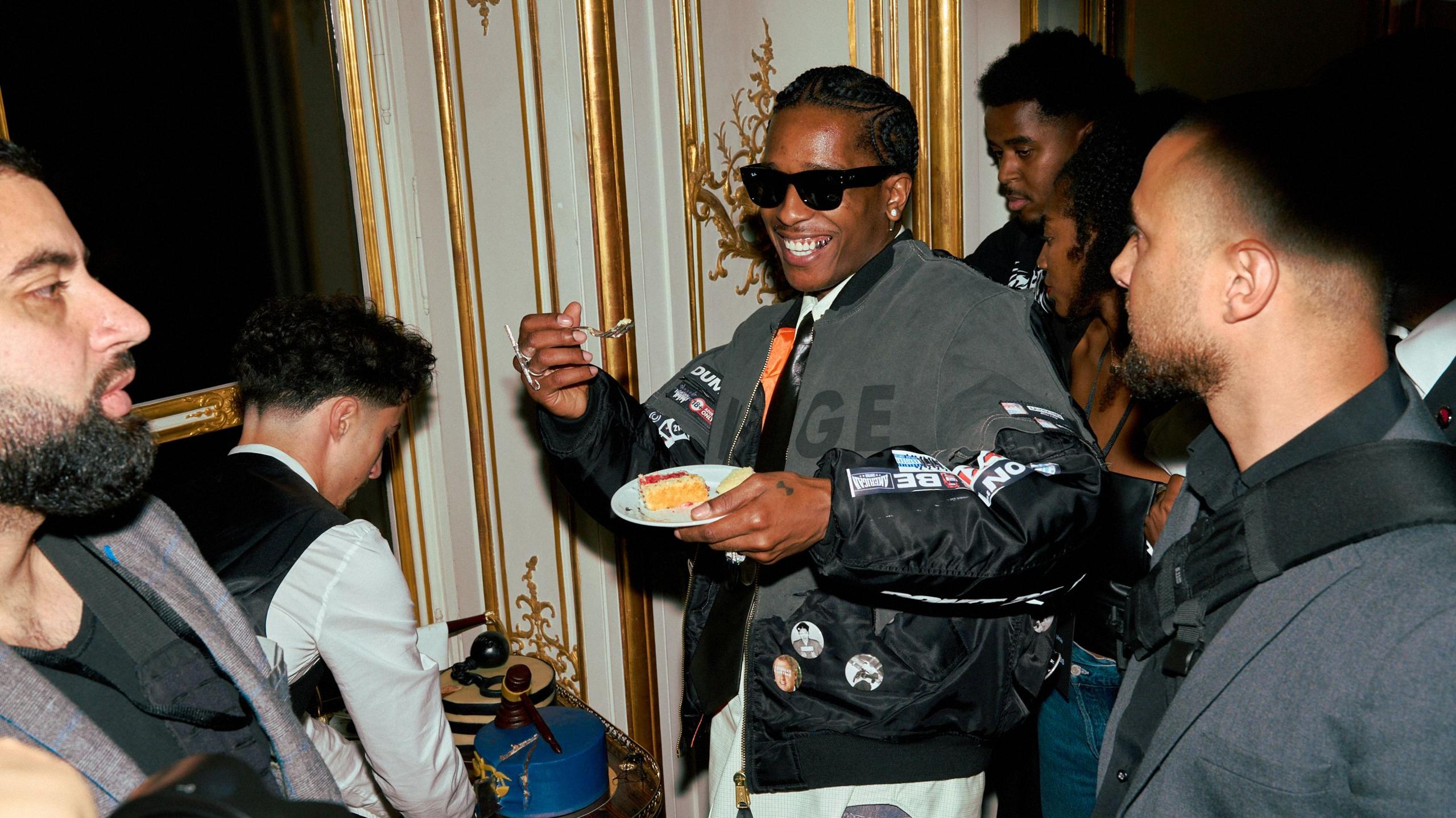 A$AP Rocky holds up slice of cake, wearing sunglasses and smiling