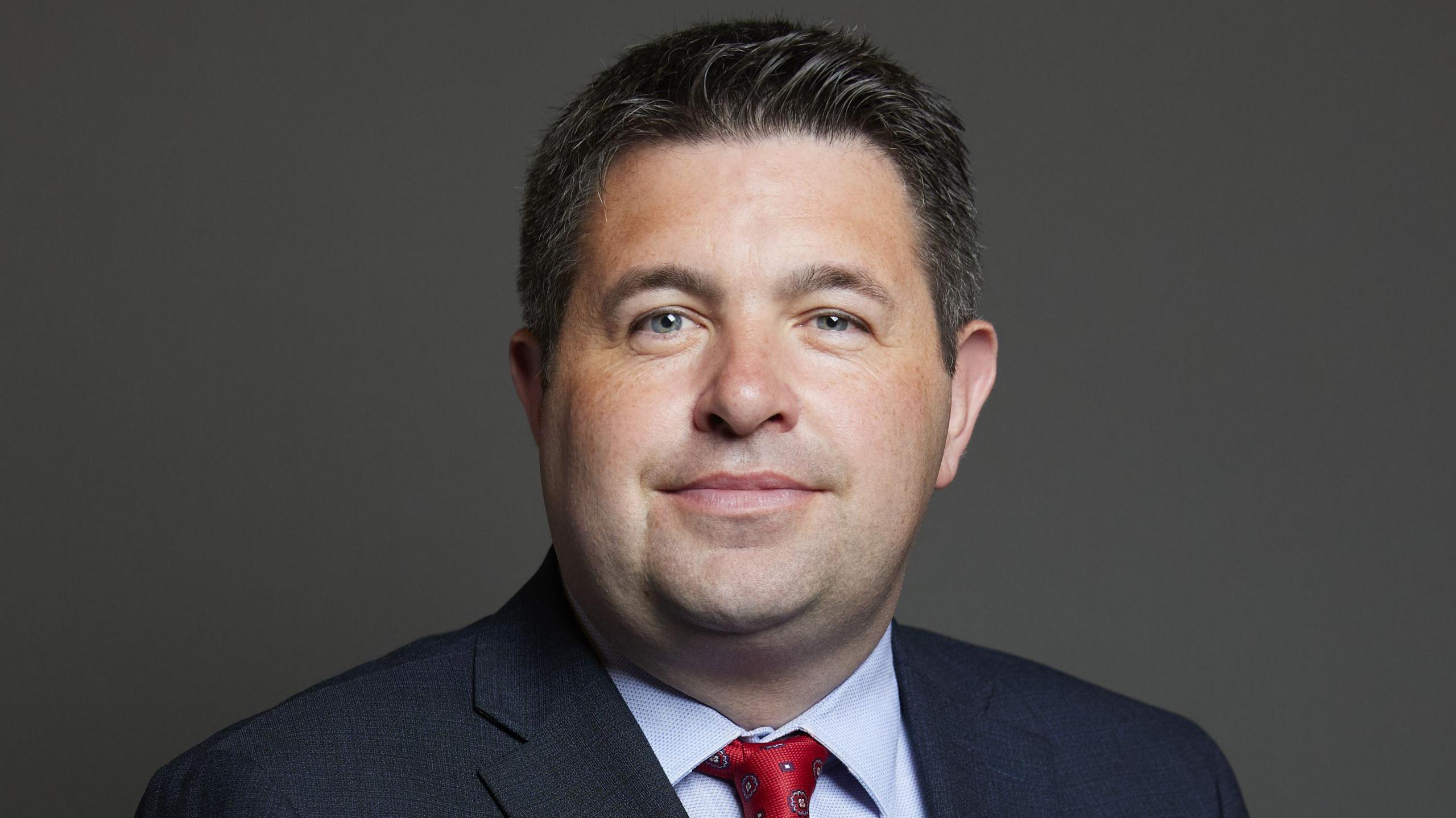 MP posing for official House of Commons photo against a plain, dark background