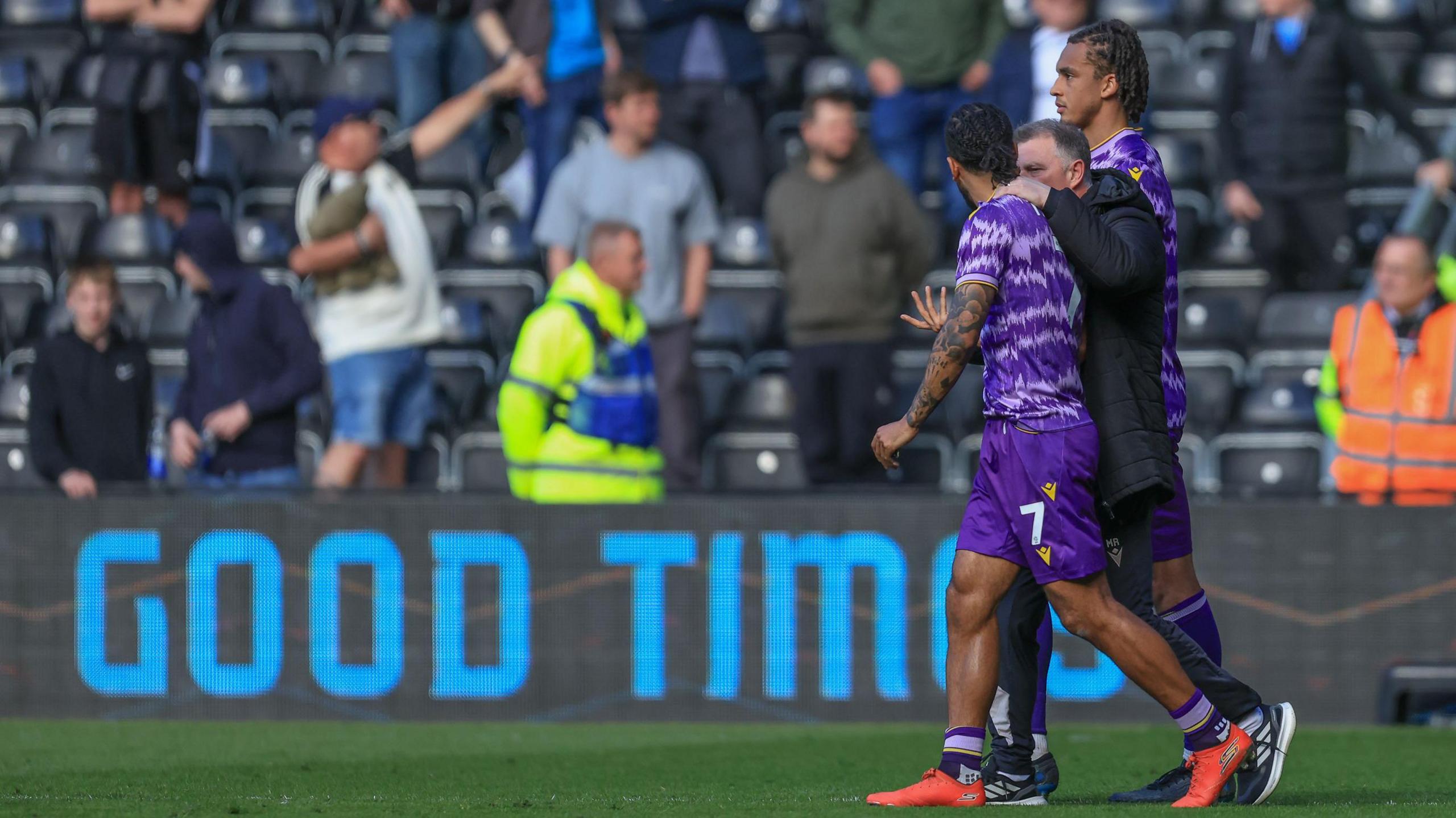 Mark Robins puts his arm around Sorba Thomas as the pair walk infront of an advertising hoarding reading Good Times.