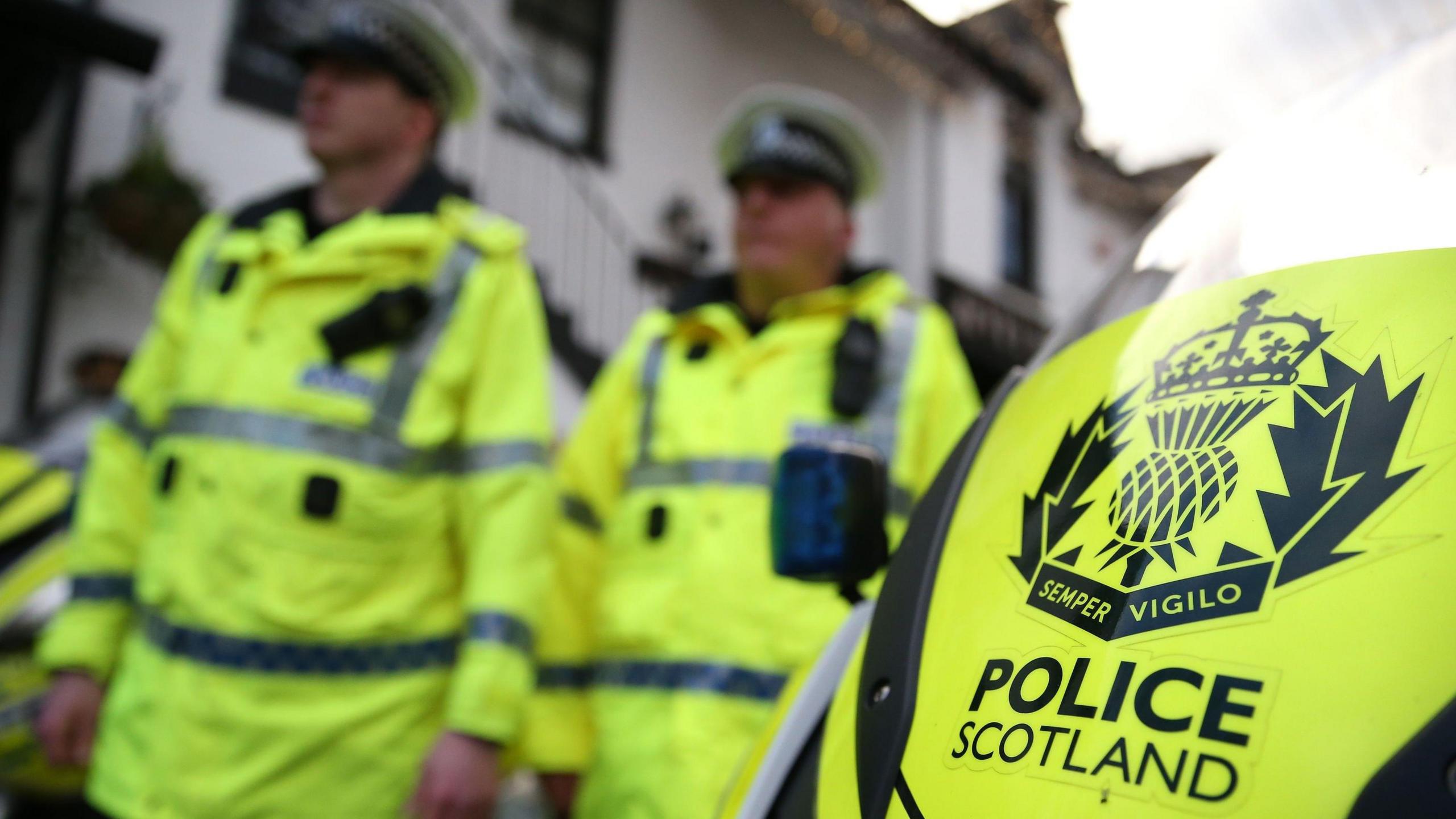 Two Police Scotland officers in uniform alongside a police motorbike