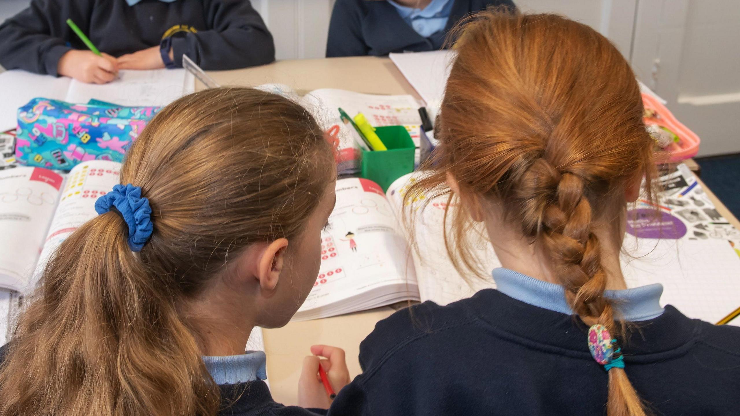 Two schoolgirls sitting at a table look at a book