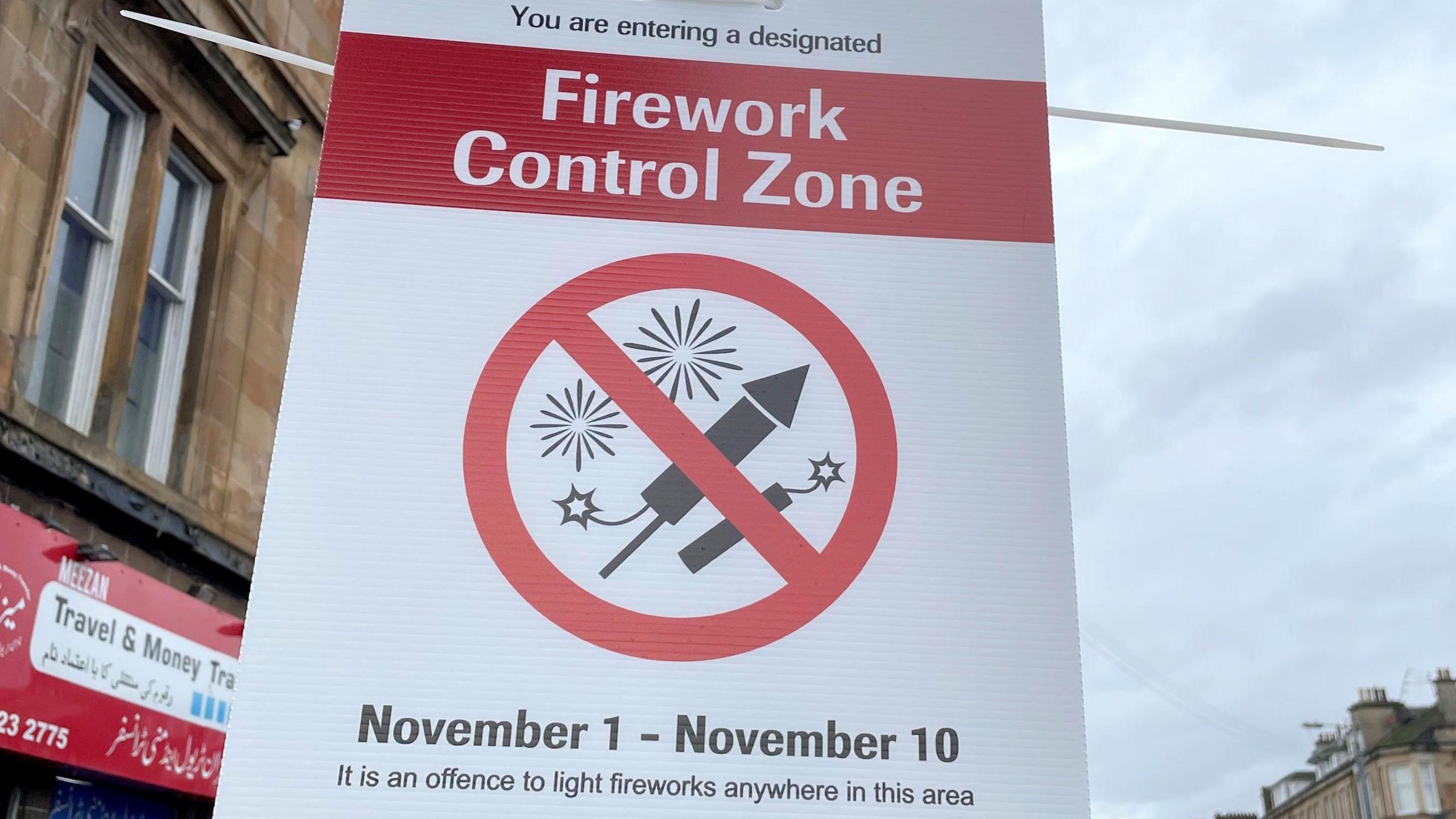 A general view of the Firework Control Zone sign located in the Pollokshields area of Glasgow. It says: "Firework Control Zone: November 1 - November 10. It is an offence to light fireworks in this area." There is a logo featuring two black and white fireworks on a white background with a red circle around it and a red strike through the middle.