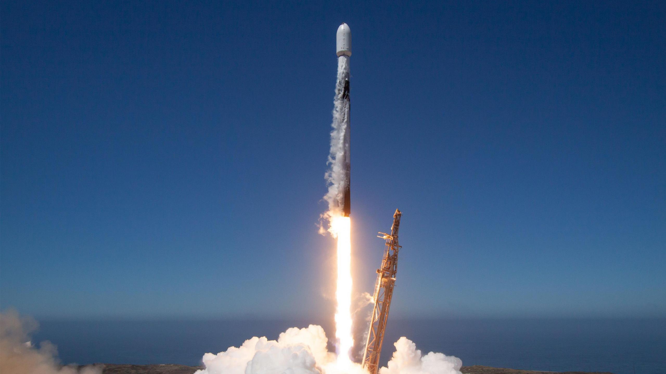 A satellite being launched into the space by a Space X rocket on a blue clear day.