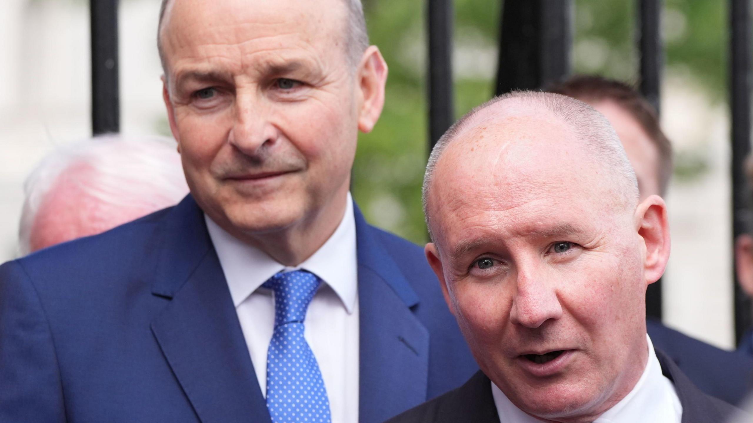 Micheál Martin and Jim Gavin outside the gates of Leinster House in Dublin earlier this month. Both men have short, grey, receding hair. Martin is wearing a blue suit and tie and Gavin is wearing a black suit with a green tie.
