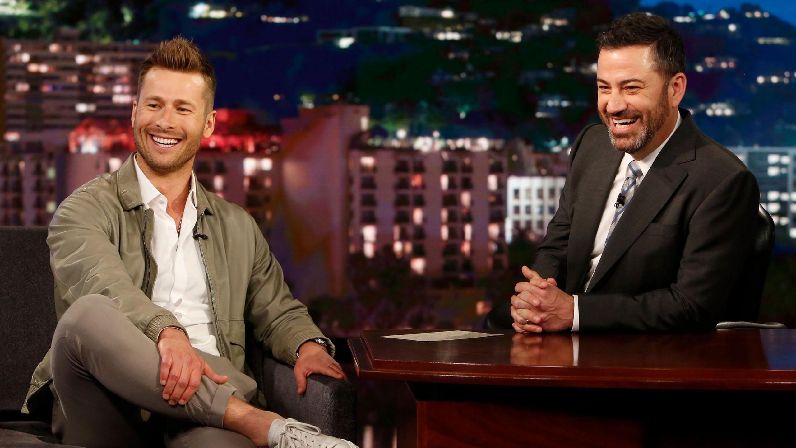 Glen Powell and Jimmy Kimmel laughing on the set of the latter's show in 2018
