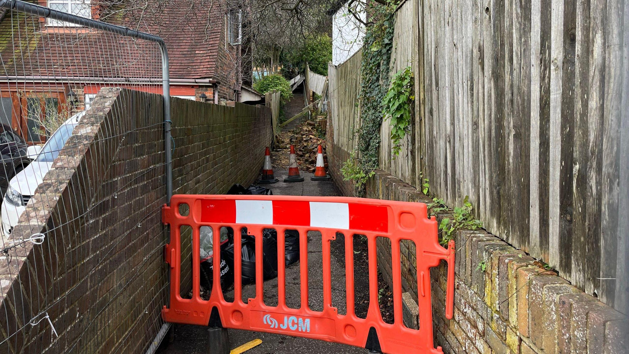 The footpath in Woodland Drive with fencing up to stop people walking up it. Fallen bricks can be seen further up the path which leads to the Three Cornered Copse woodland