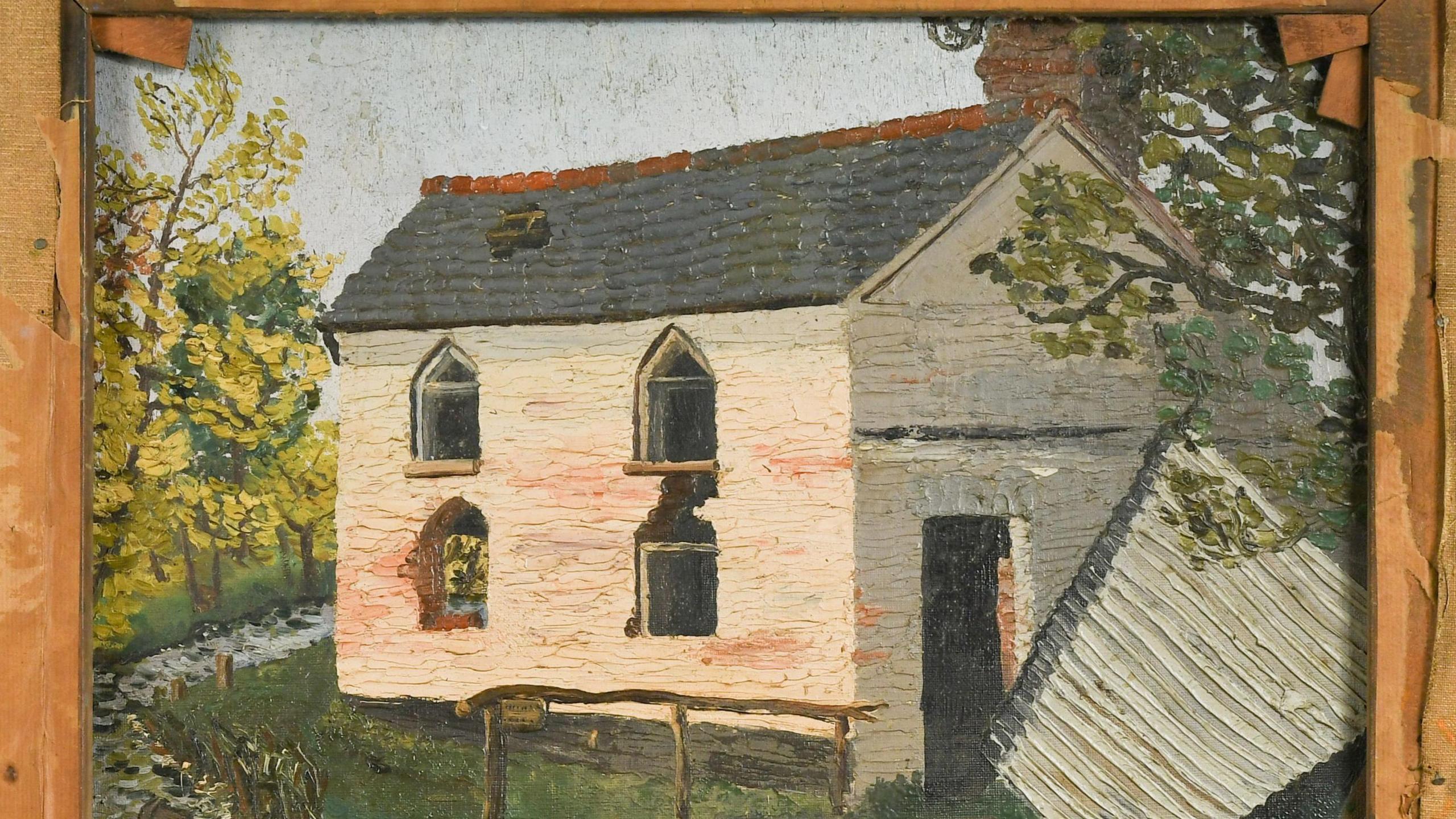 The reverse side of another painting in a wooden frame shows a run down home in the country. It is white, with chipped paint, missing glass in the windows and has a hole in the roof. There are some trees, grass and a little stream around the building.  