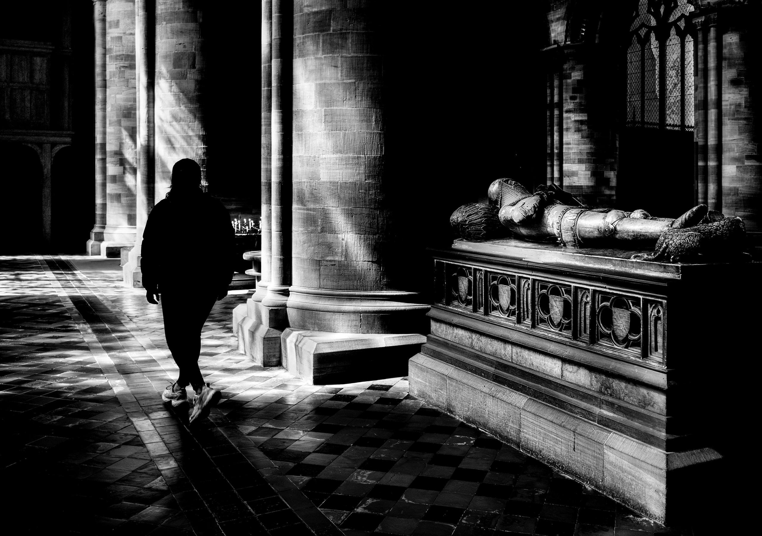 A figure walks past a tomb in a cathedral