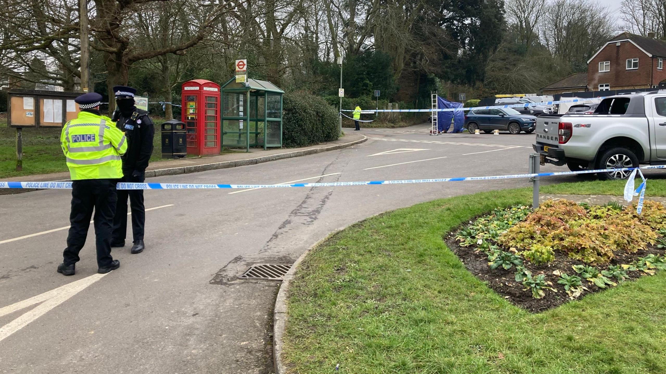 A road in the village of Knockholt with two police officers and a police tape cordon