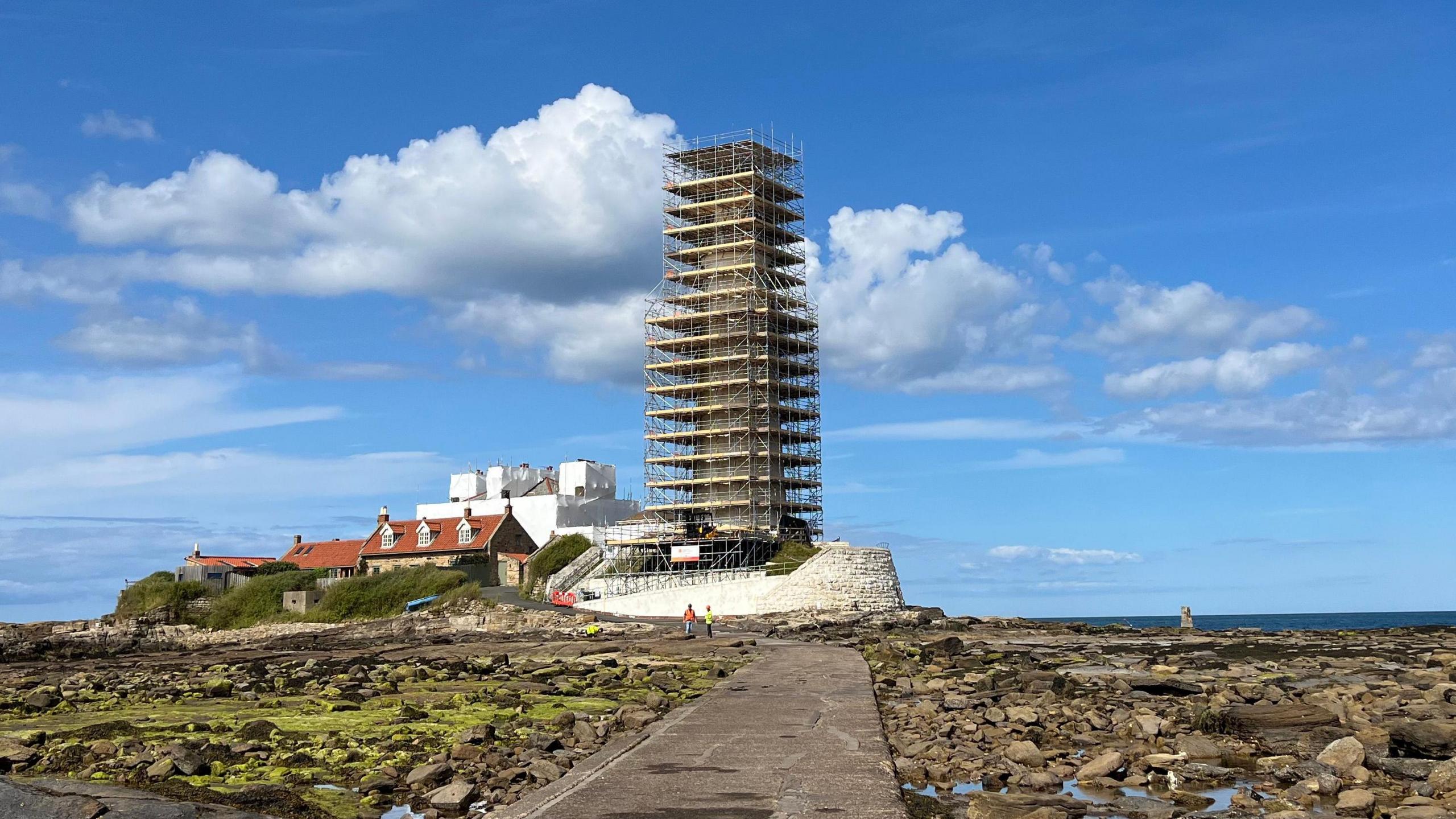 A lighthouse on an island, surrounded by scaffolding.