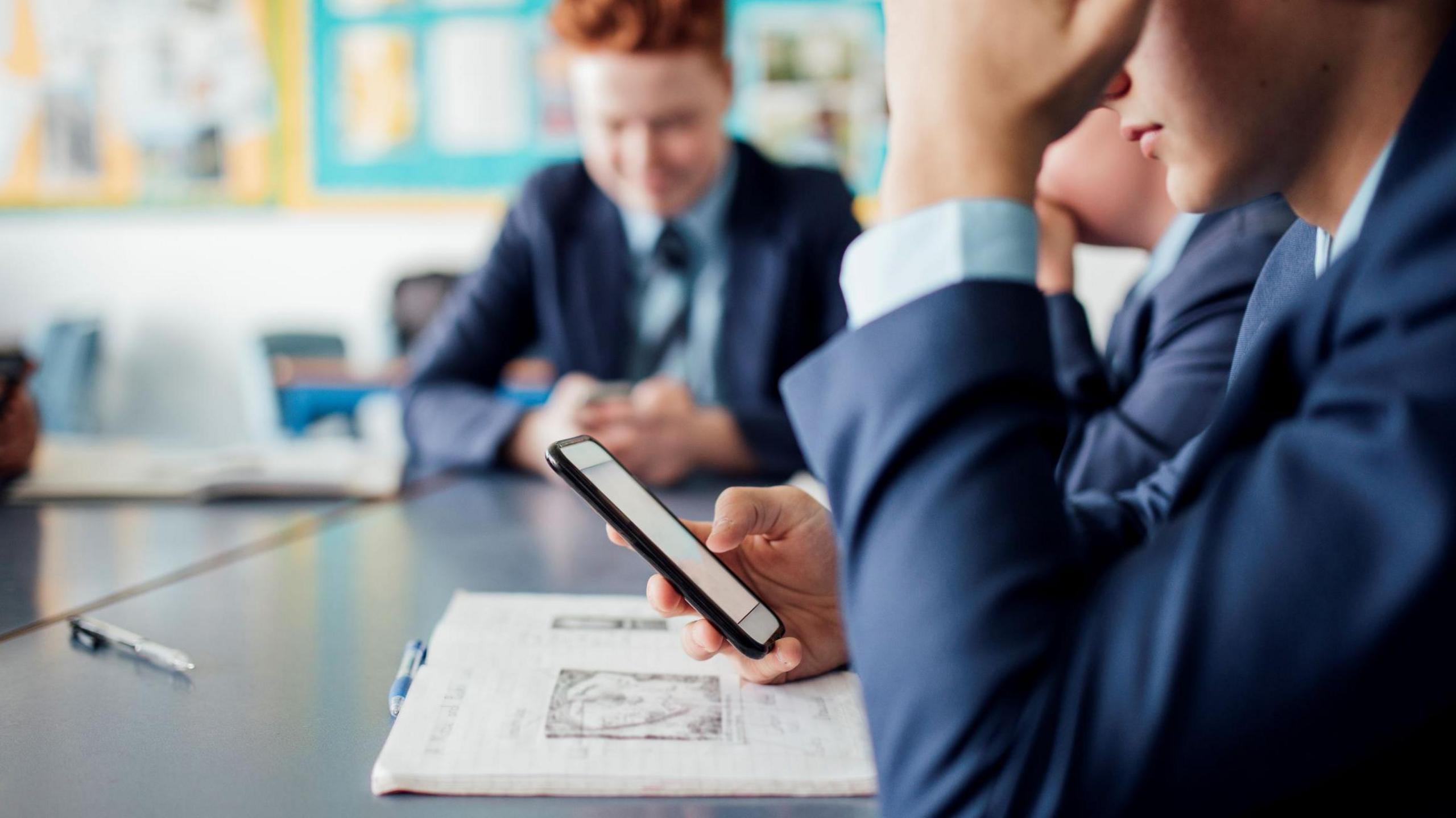 The picture shows a classroom full of young boys all looking at mobile phones. 