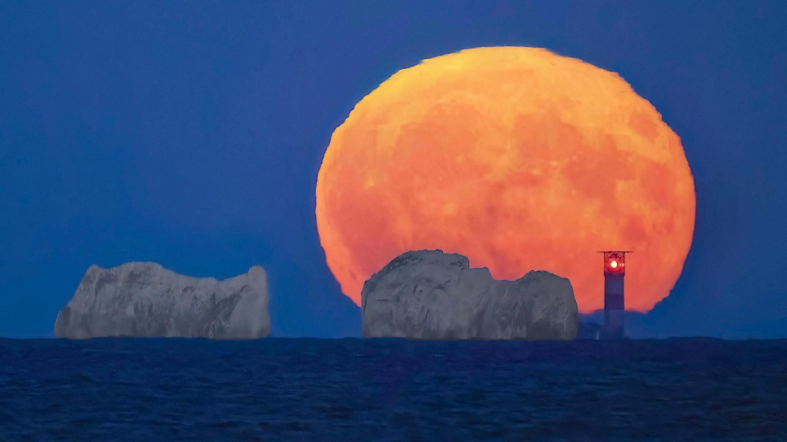 Large orange moon behind The Needles cliffs and lighthouse