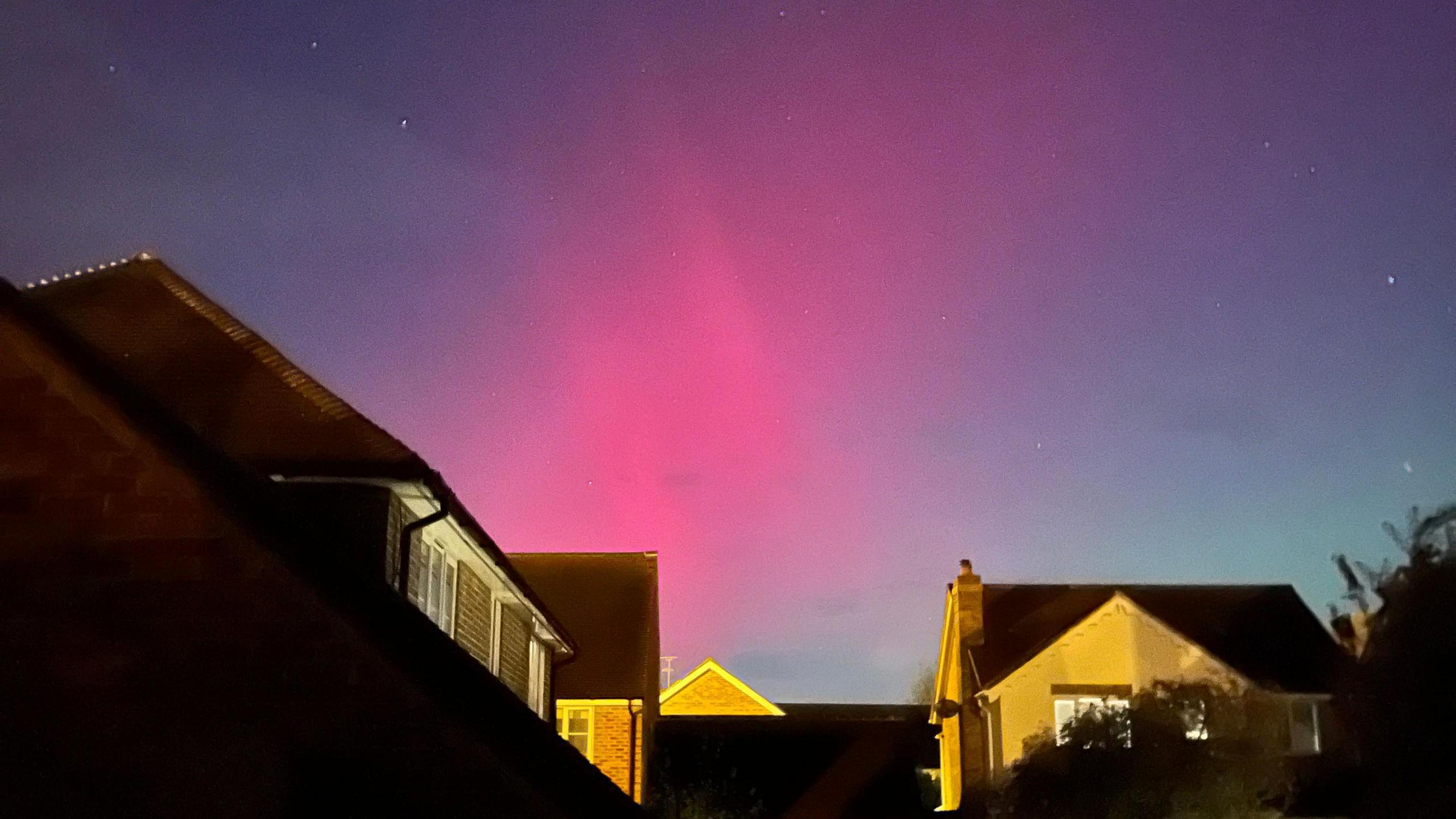 A pink light is in the night sky above houses