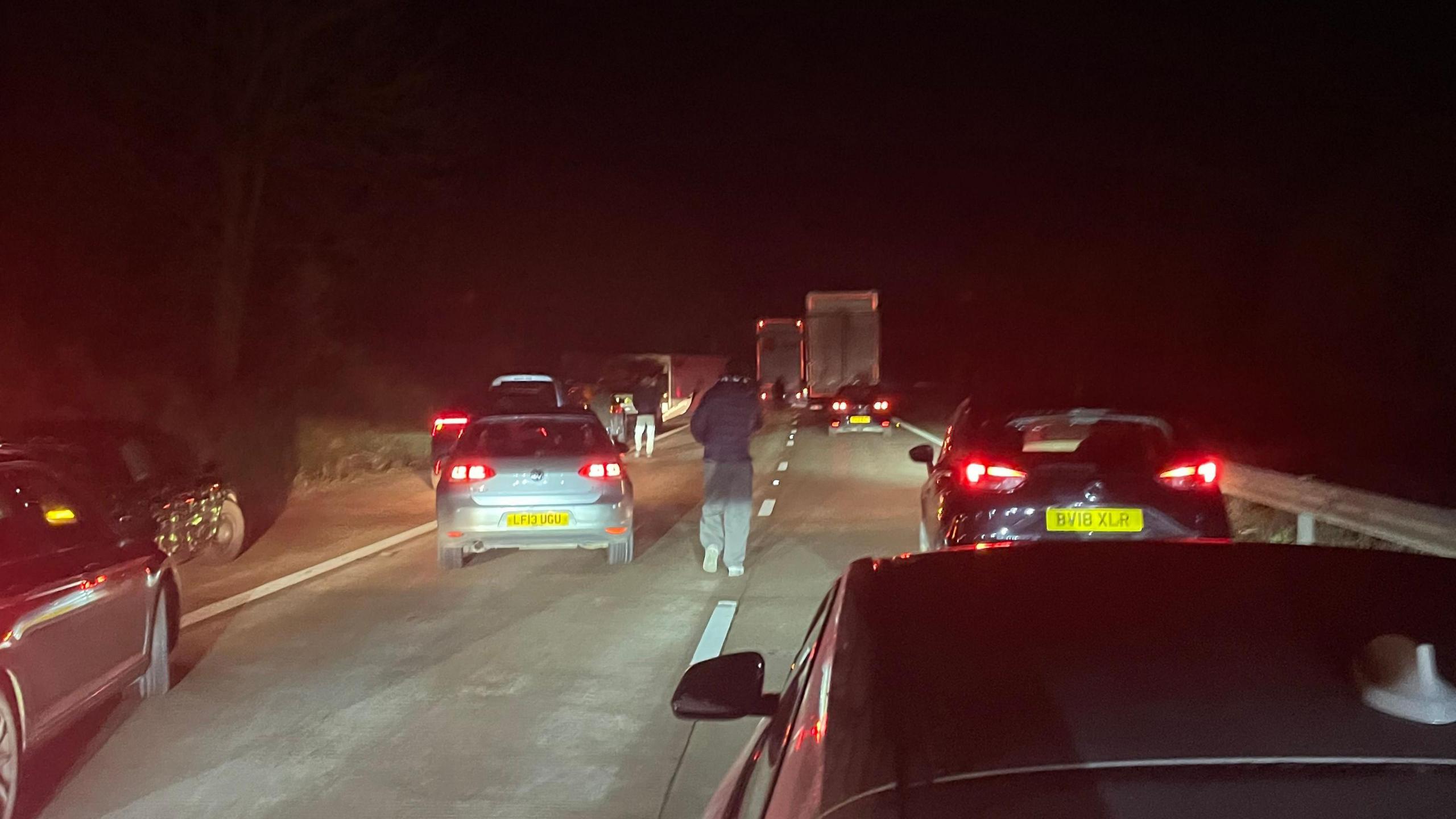 Cars stopped on a motorway with people standing outside their cars, at night