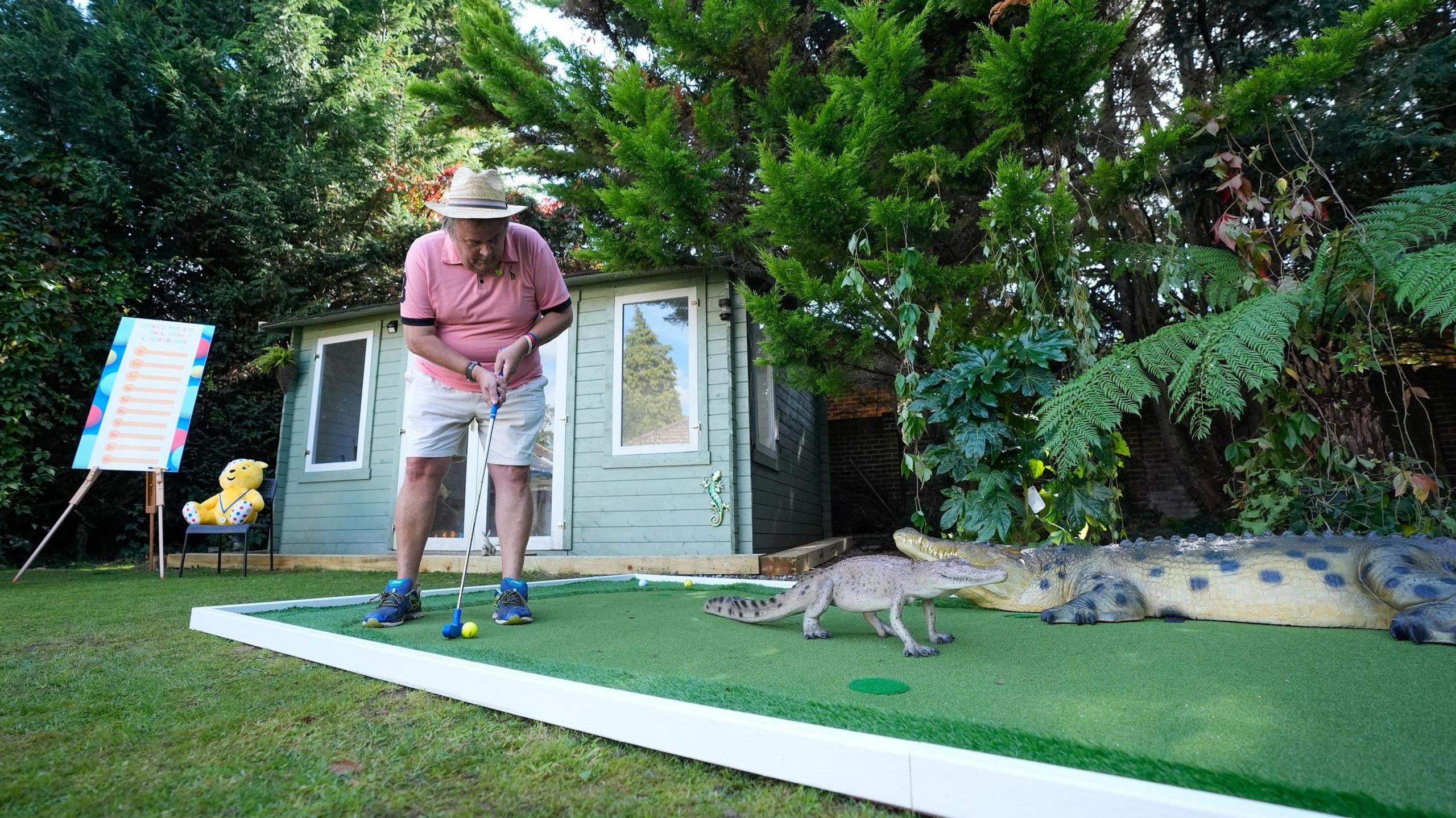 David Lawrence plays a shot on his jungle themed hole which has a model alligator and crocodile, with a garden shed and Pudsey Bear visible in the background