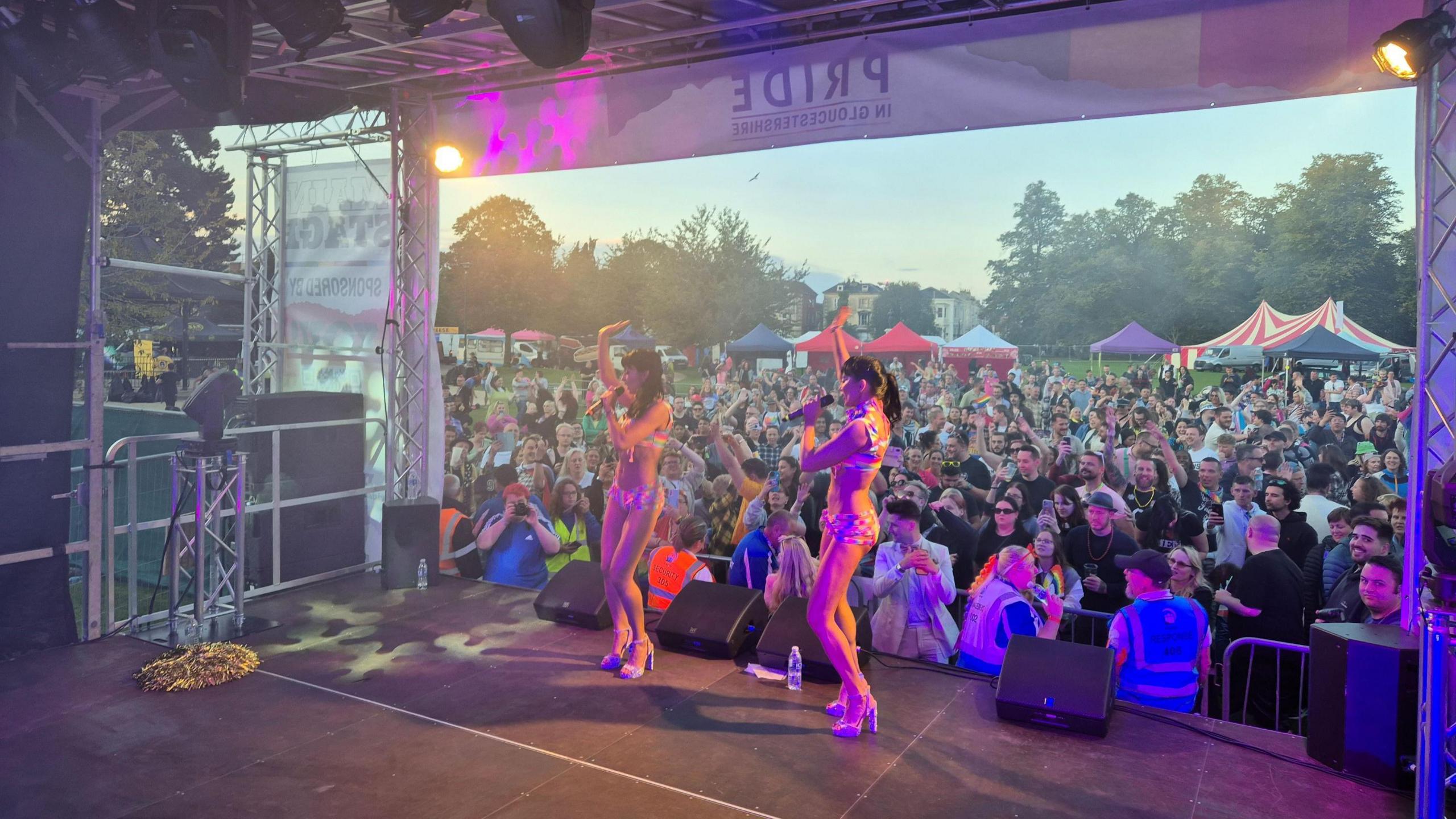 The Cheeky Girls onstage with their hands in the air performing to a crowd in a field