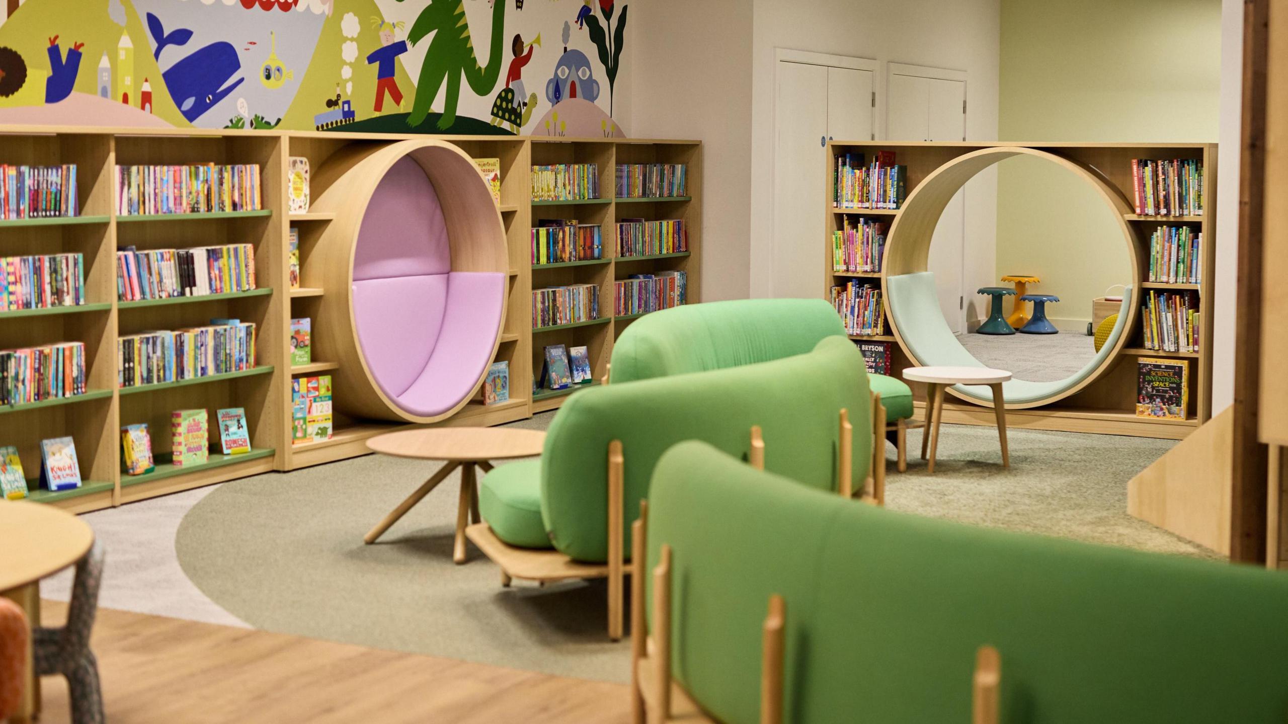 A children's learning area with colourful furniture, book-lined walls and murals on the walls