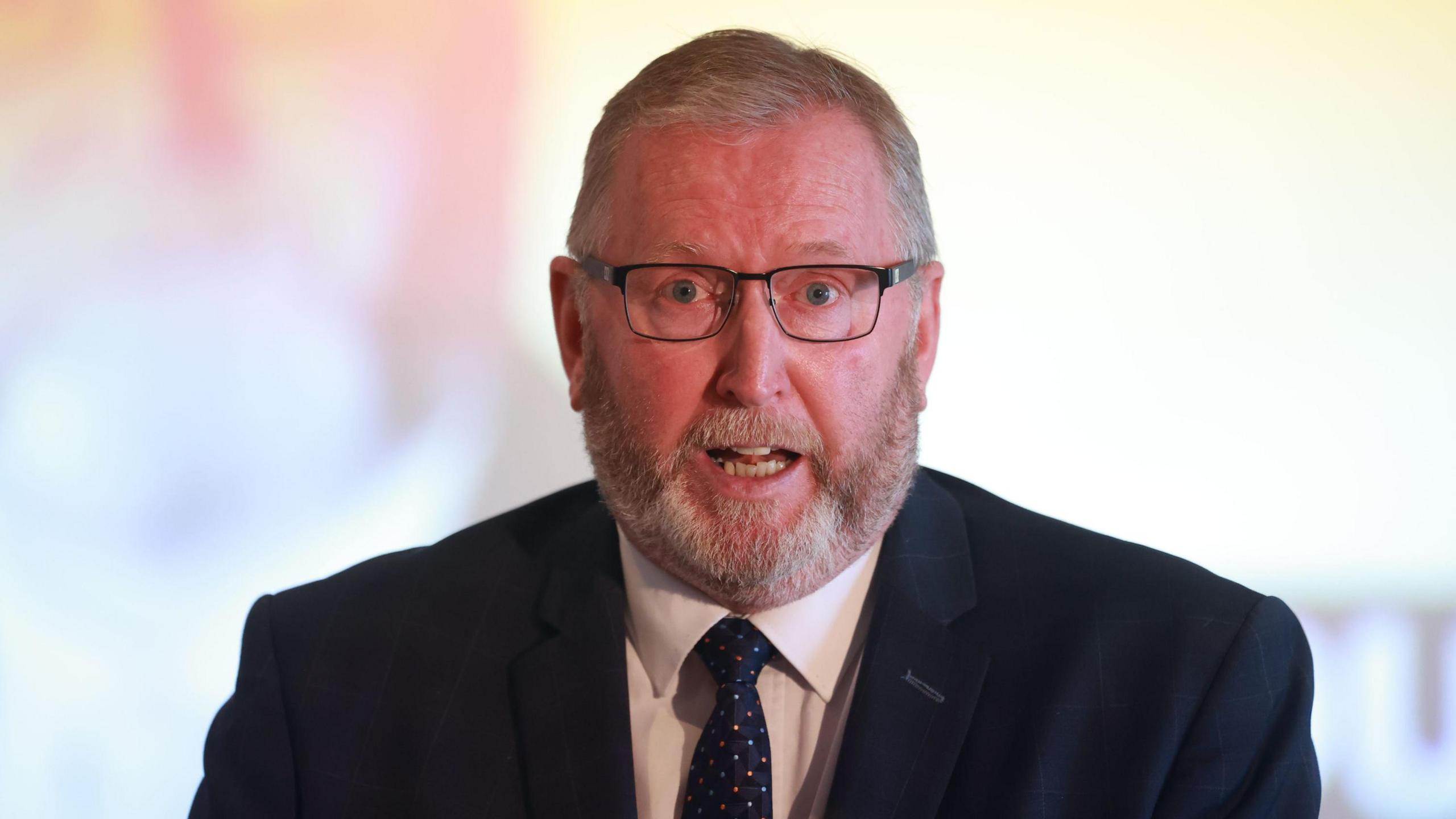 Headshot of Doug Beattie speaking. He is wearing a suit and tie. The background is out of focus.