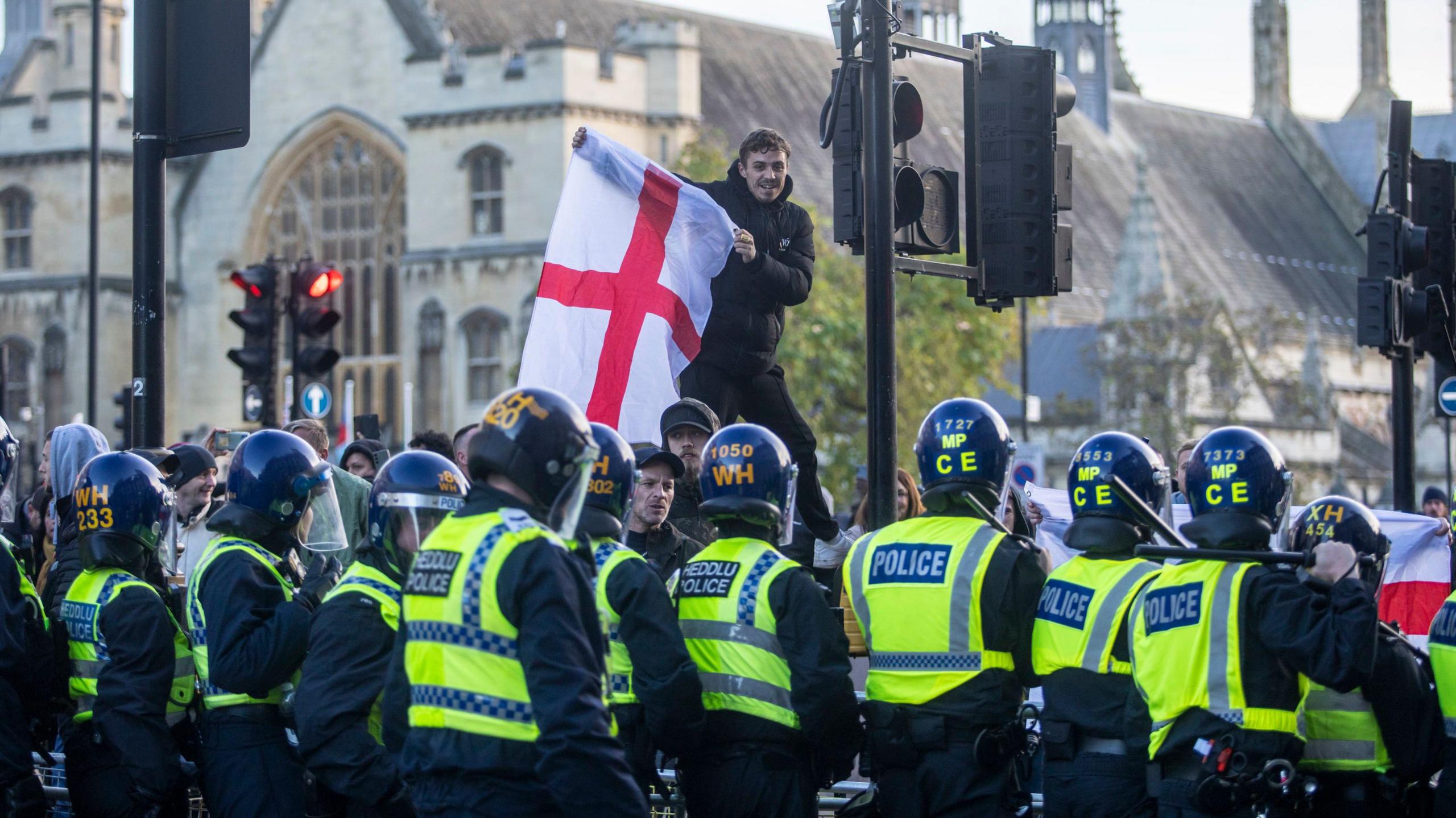 Row of policer officers in riot gear and counter protester with England flag