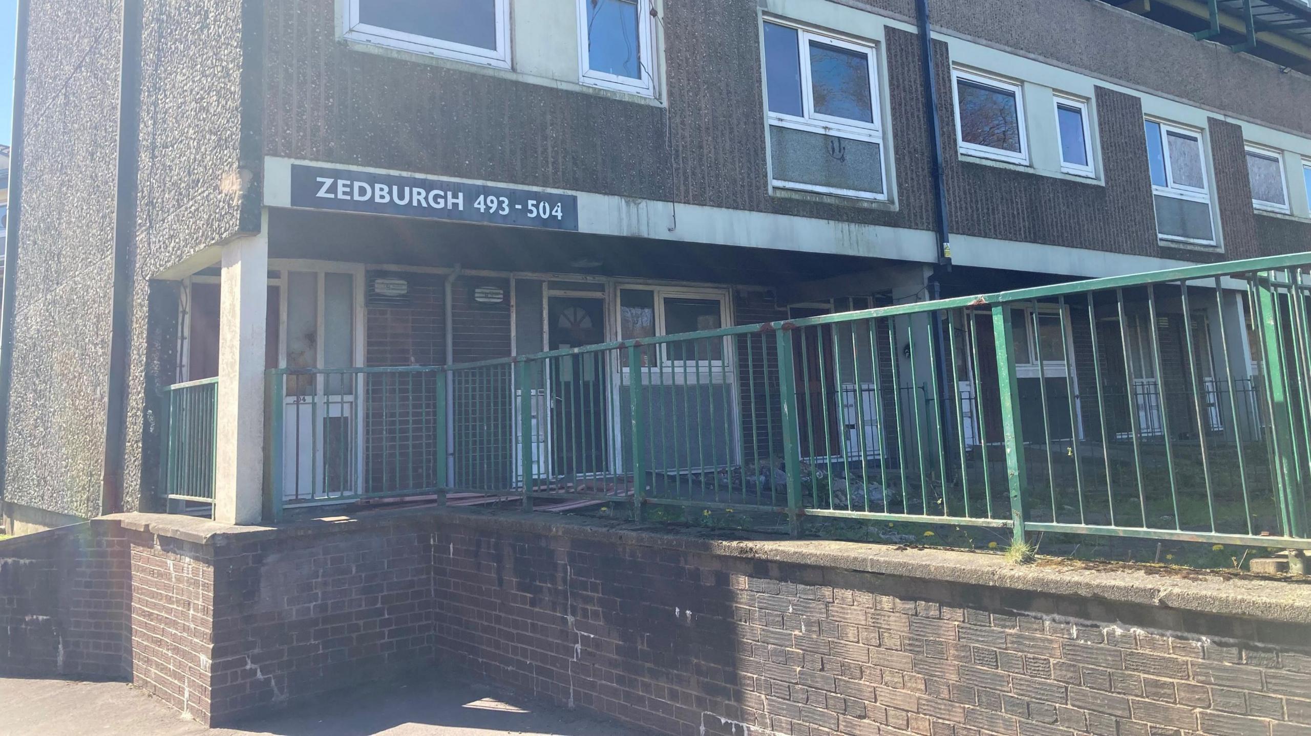Zedburgh block on the the Lower Falinge estate in Rochdale. It is a 1970s brick building with white windows and green railings