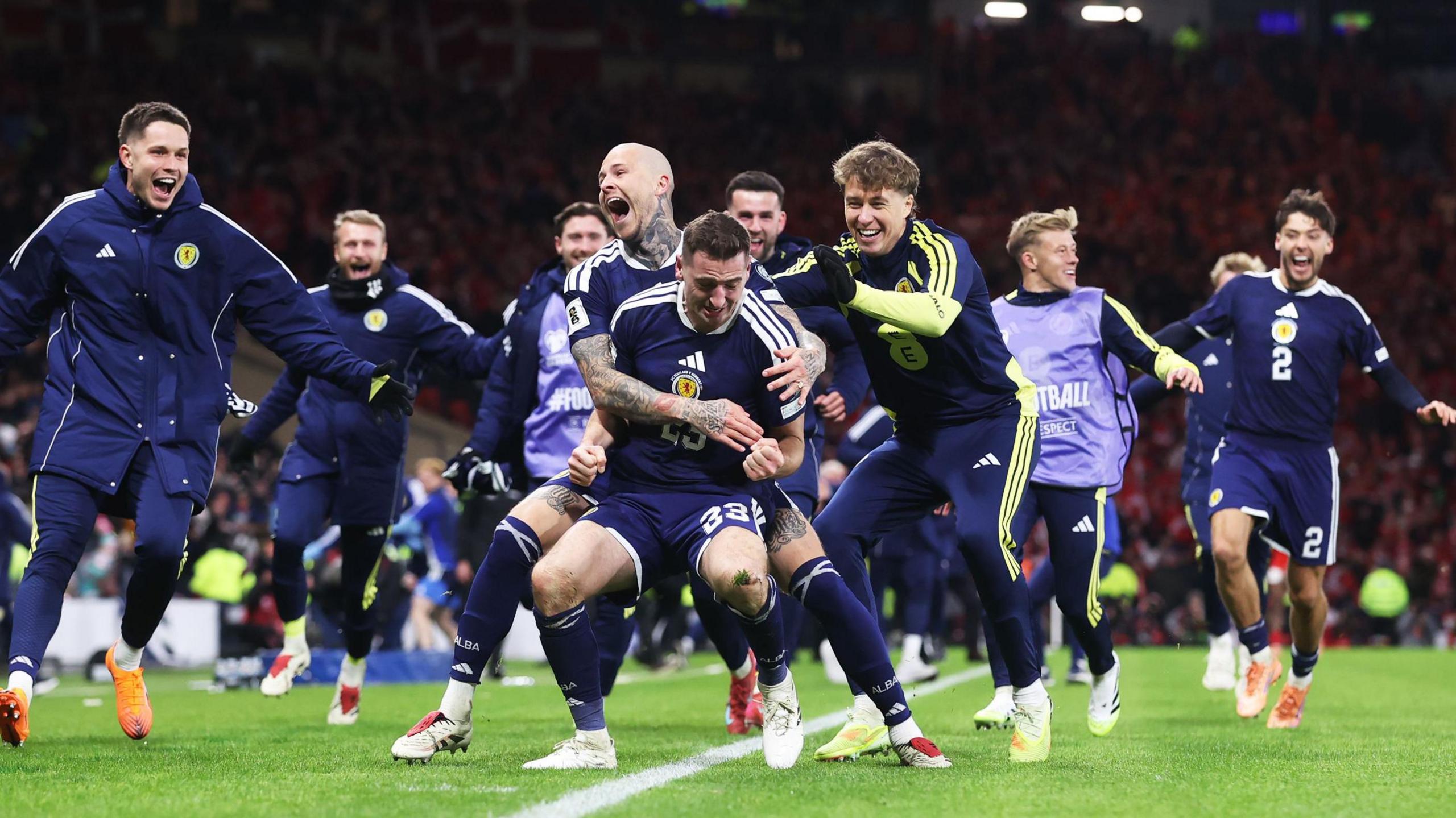 Scotland players wearing dark blue shirts celebrating with Kenny McLean during Scotland's win over Denmark.