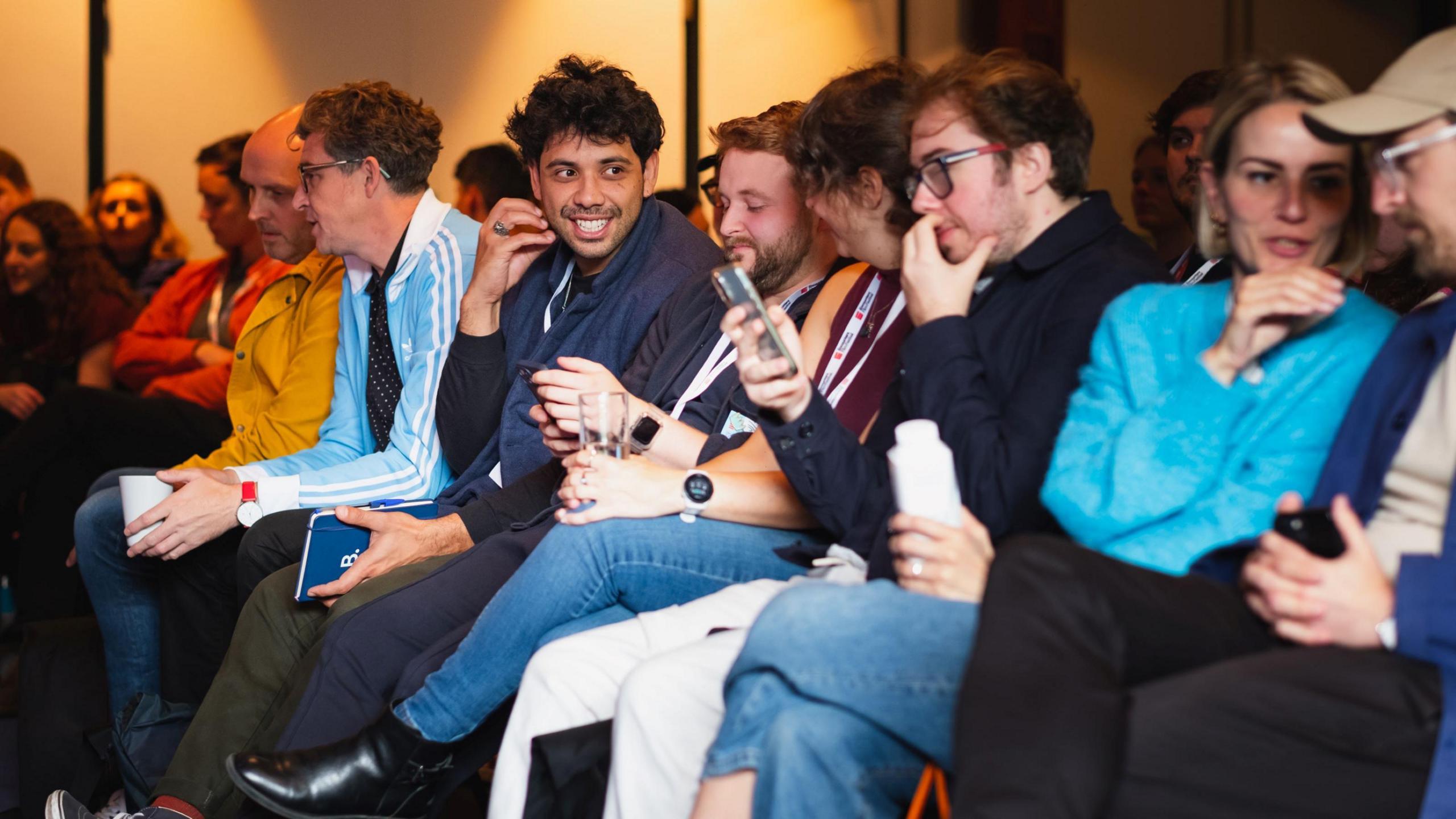 A row of young people sitting together in rowed seating at the Encounters Film Festival in Bristol. They are talking among themselves and some of them are looking at their phones.