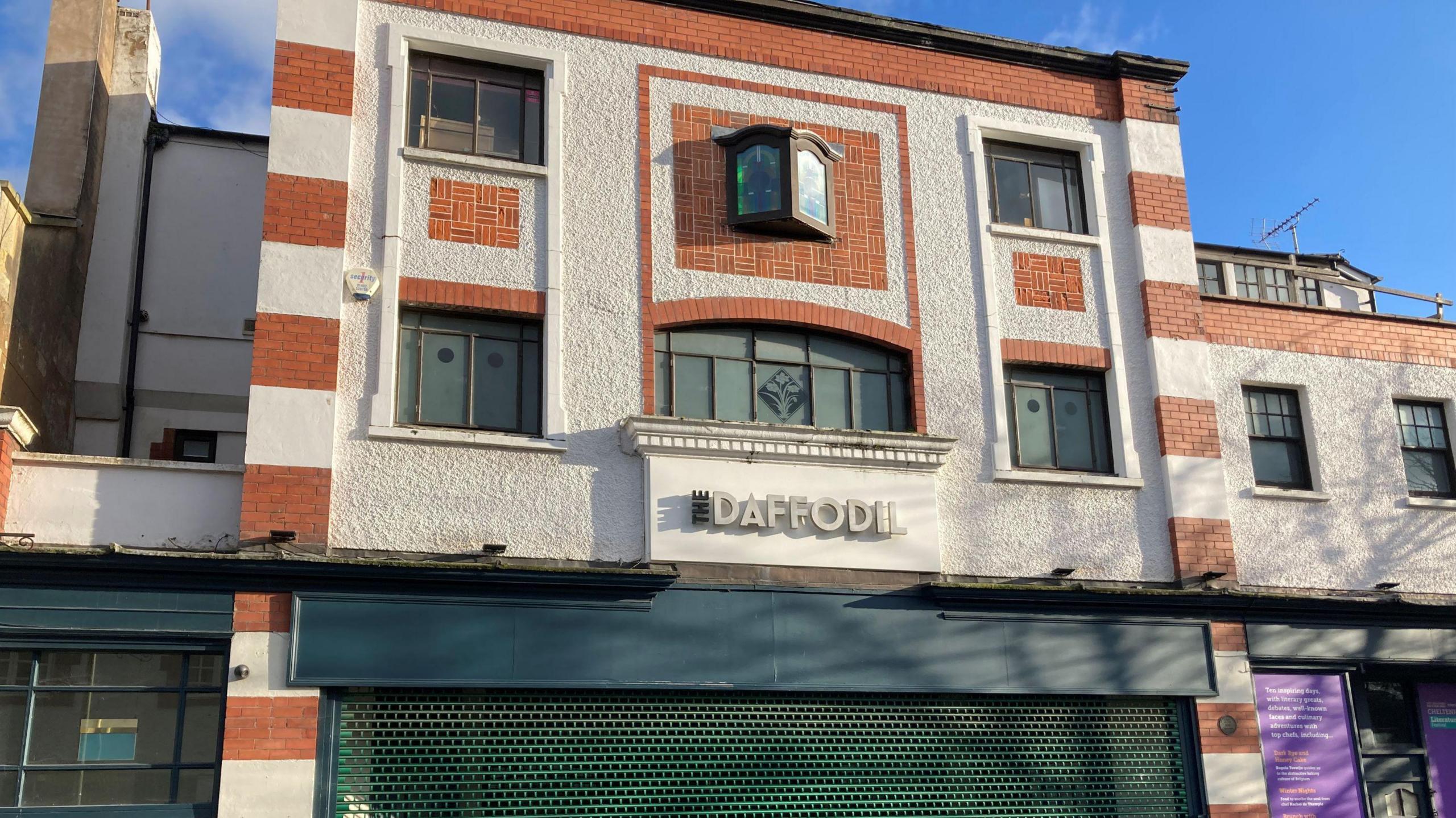 A four storey building with green shutters across the entrance is on a road with both business and residential properties