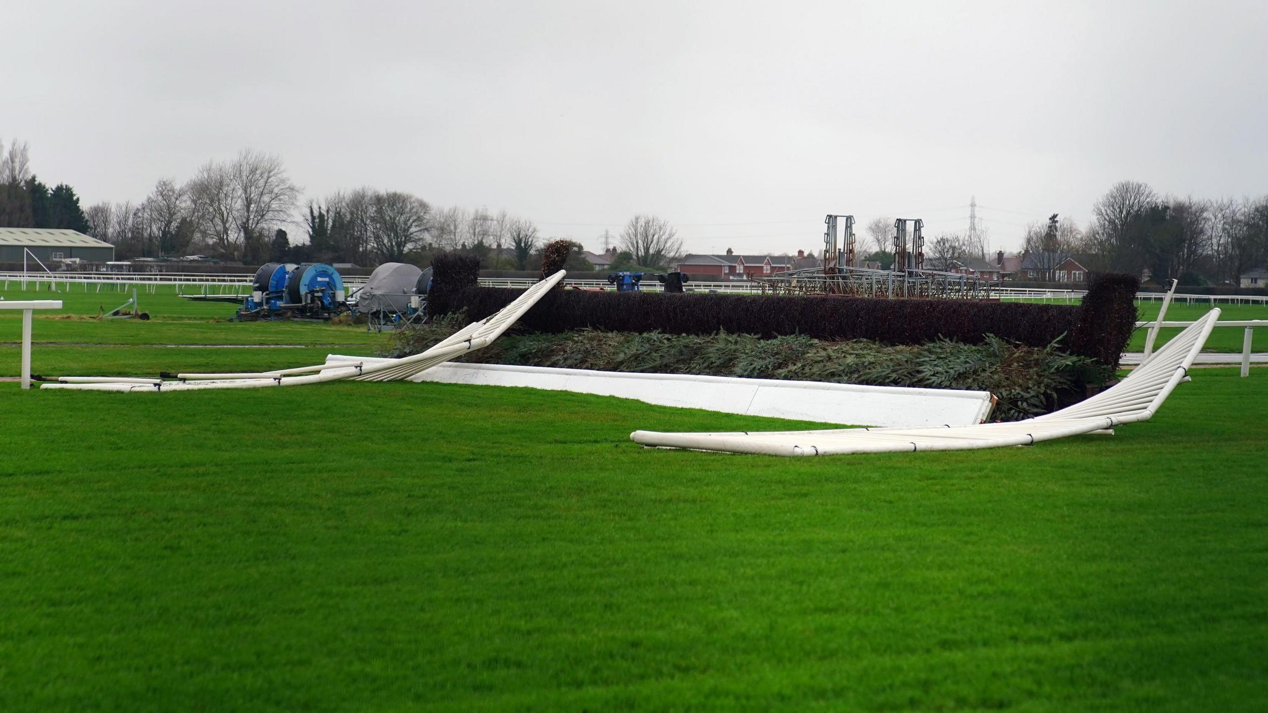 Fallen white side rails on both sides of a grassy hurdle on the green racecourse