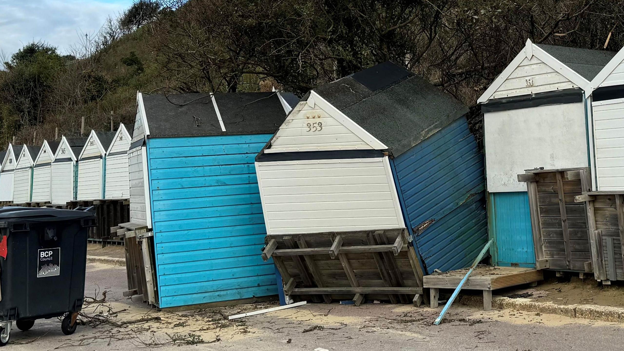 Beach huts at Durley Chine, which are wooden with pointed roofs. Behind them is a cliff