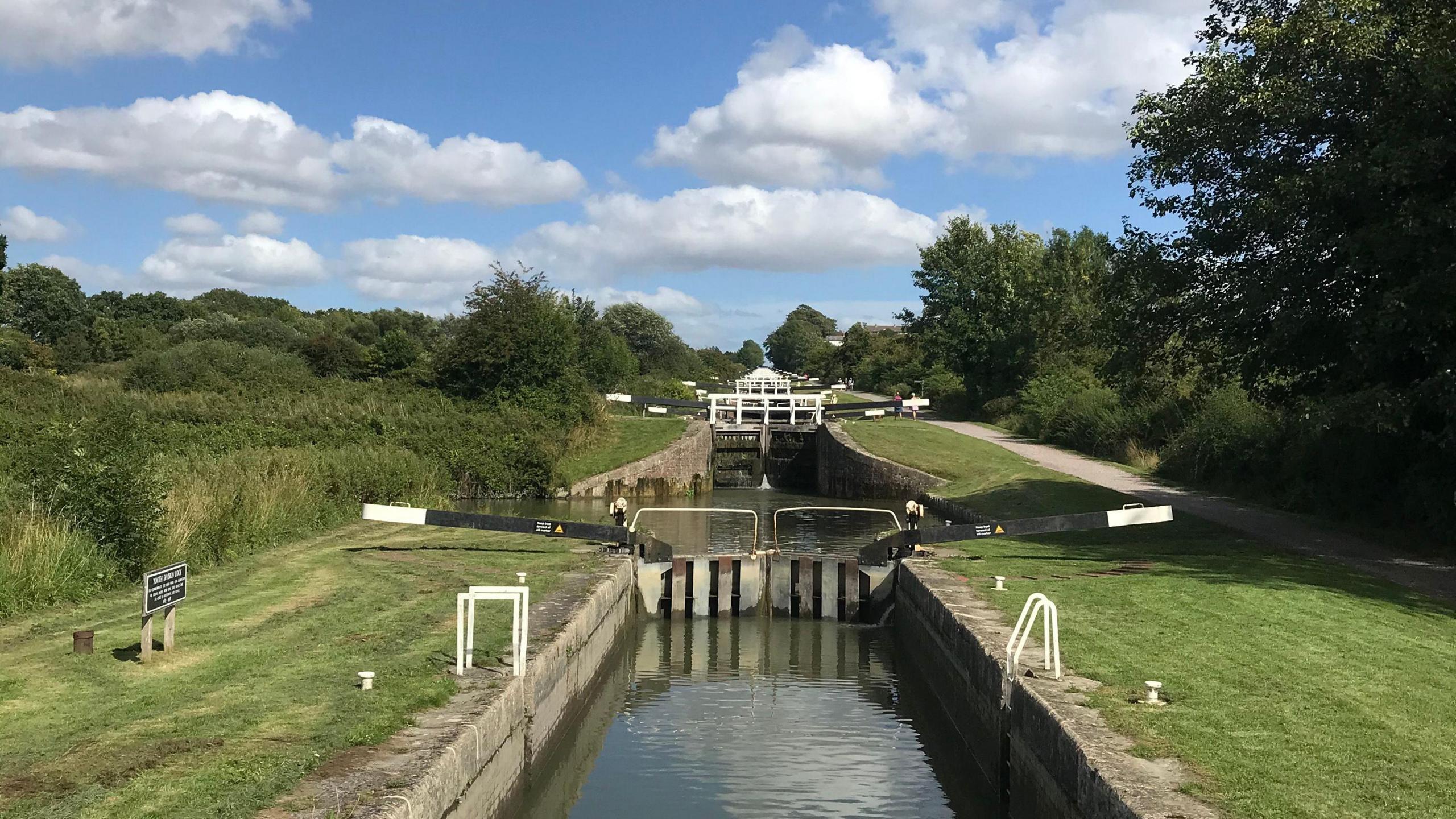 Looking down a set of canal locks under a blue sky with greenery on either side.