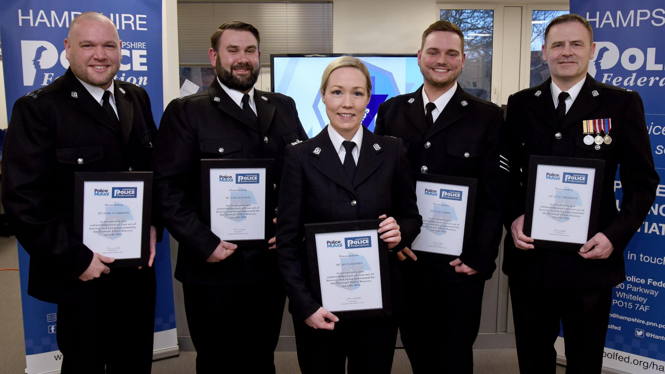 Four men and one woman in police uniforms stand holding certificates in a room 