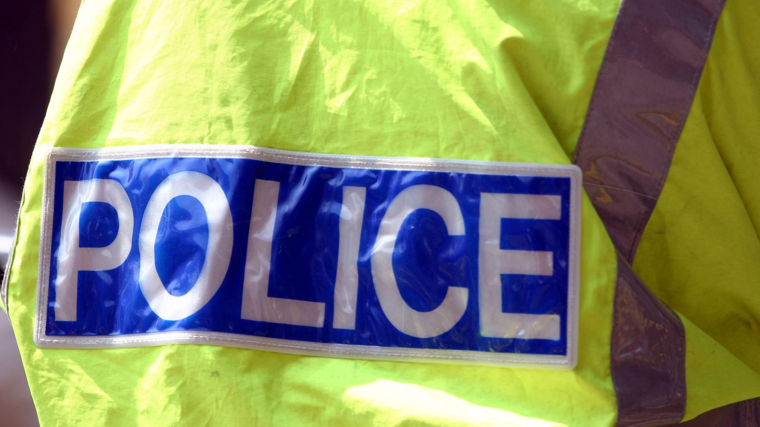 A generic photo of a police officer's distinctive fluorescent jacket. A blue badge reads: "Police"