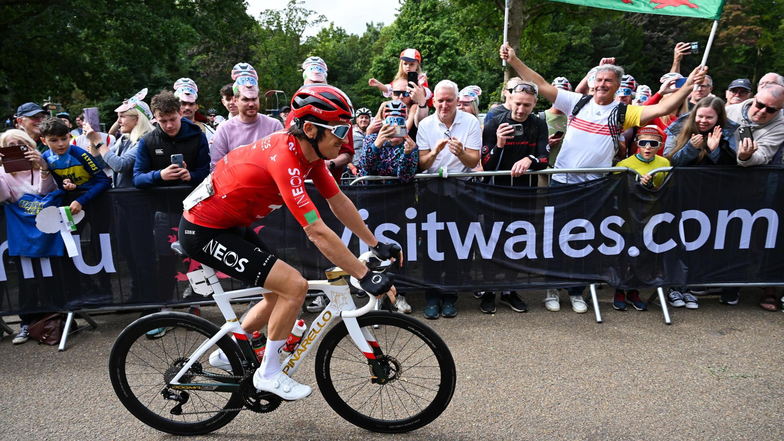 Geraint Thomas wears a red top and black shorts and he cycles past crowds of people