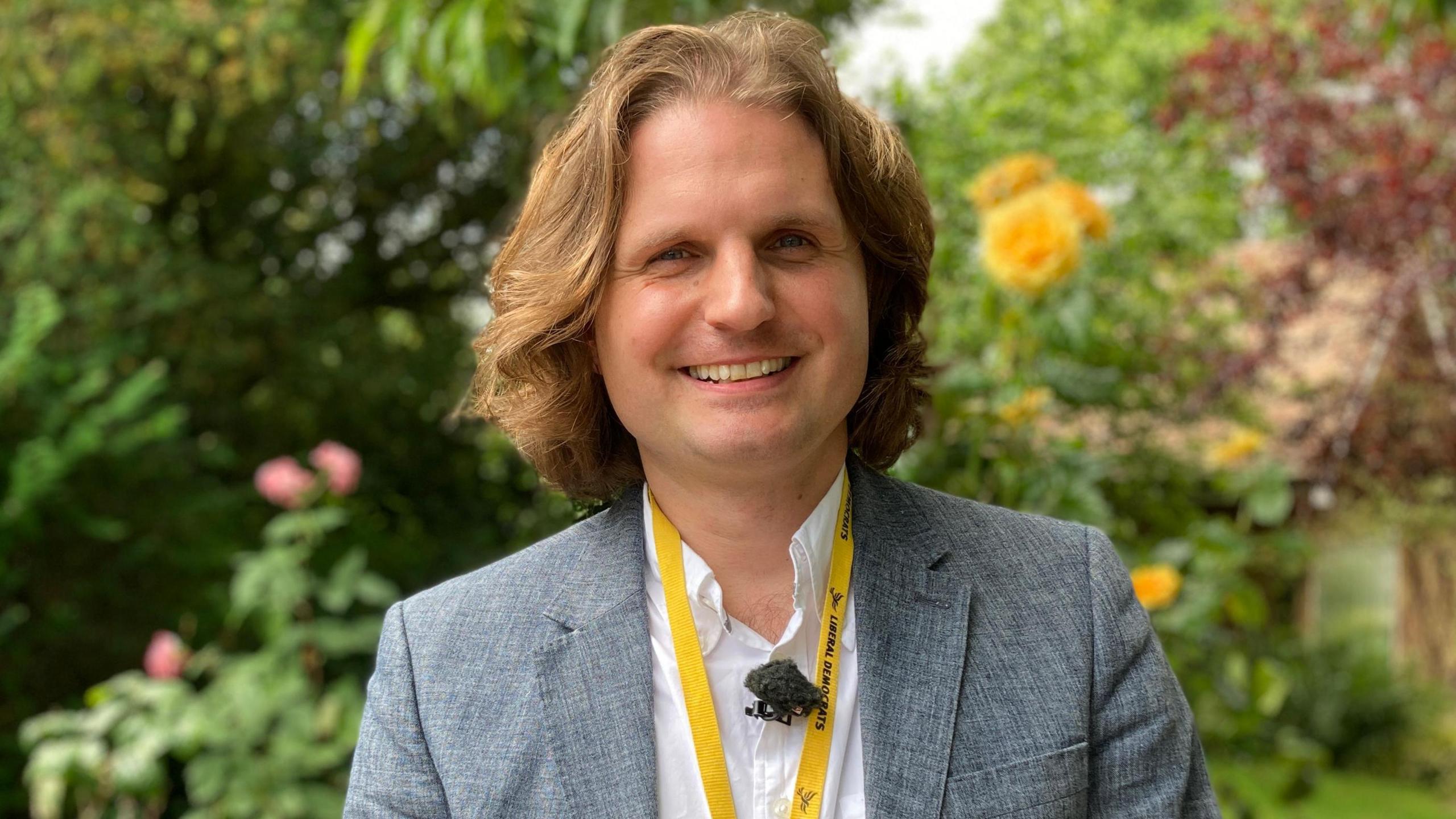 Steffan Aquarone, looking at the camera and is smiling. He is standing outside and is wearing a grey suit jacket and white shirt.